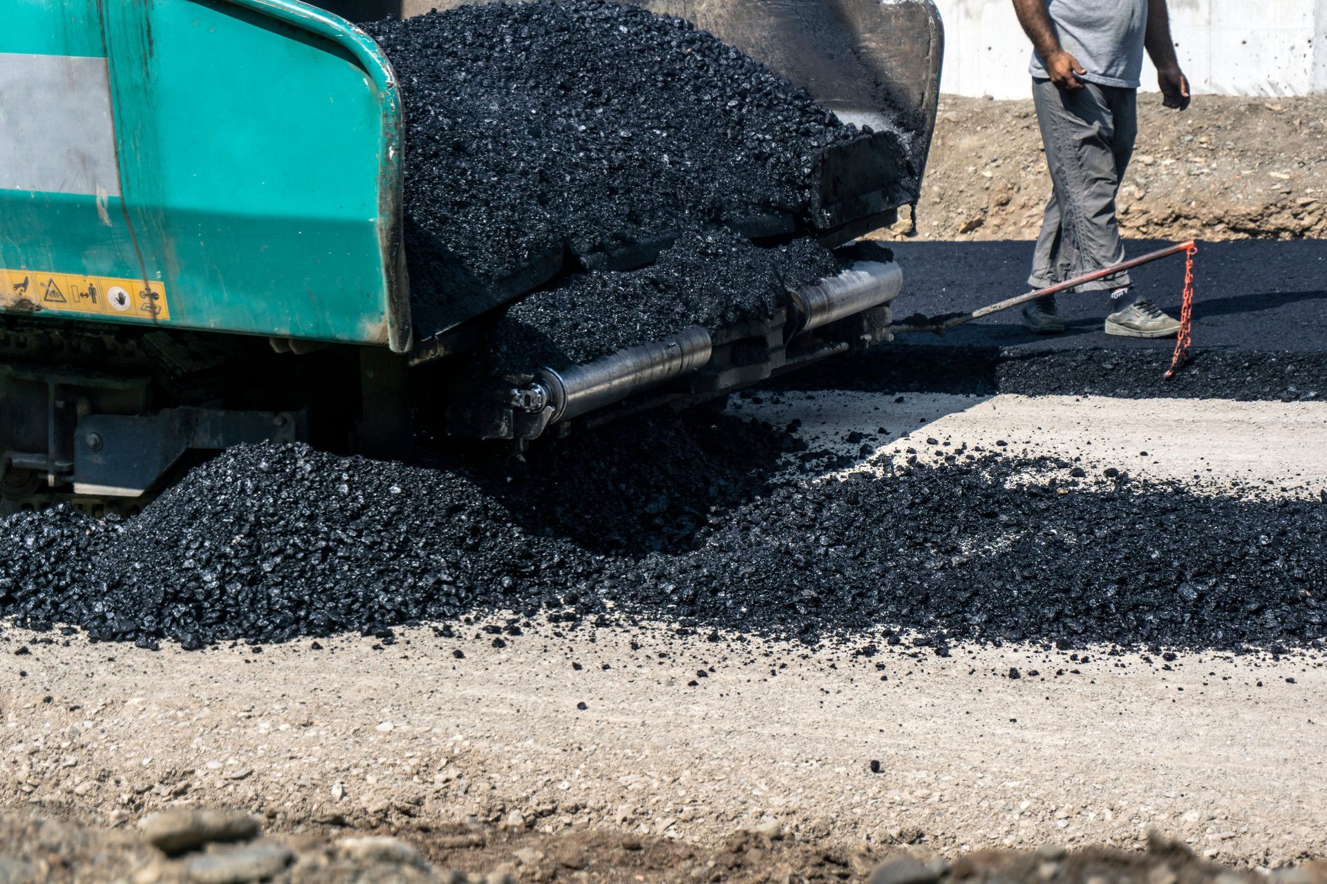 Asphalt being poured from a paving truck onto a road surface.