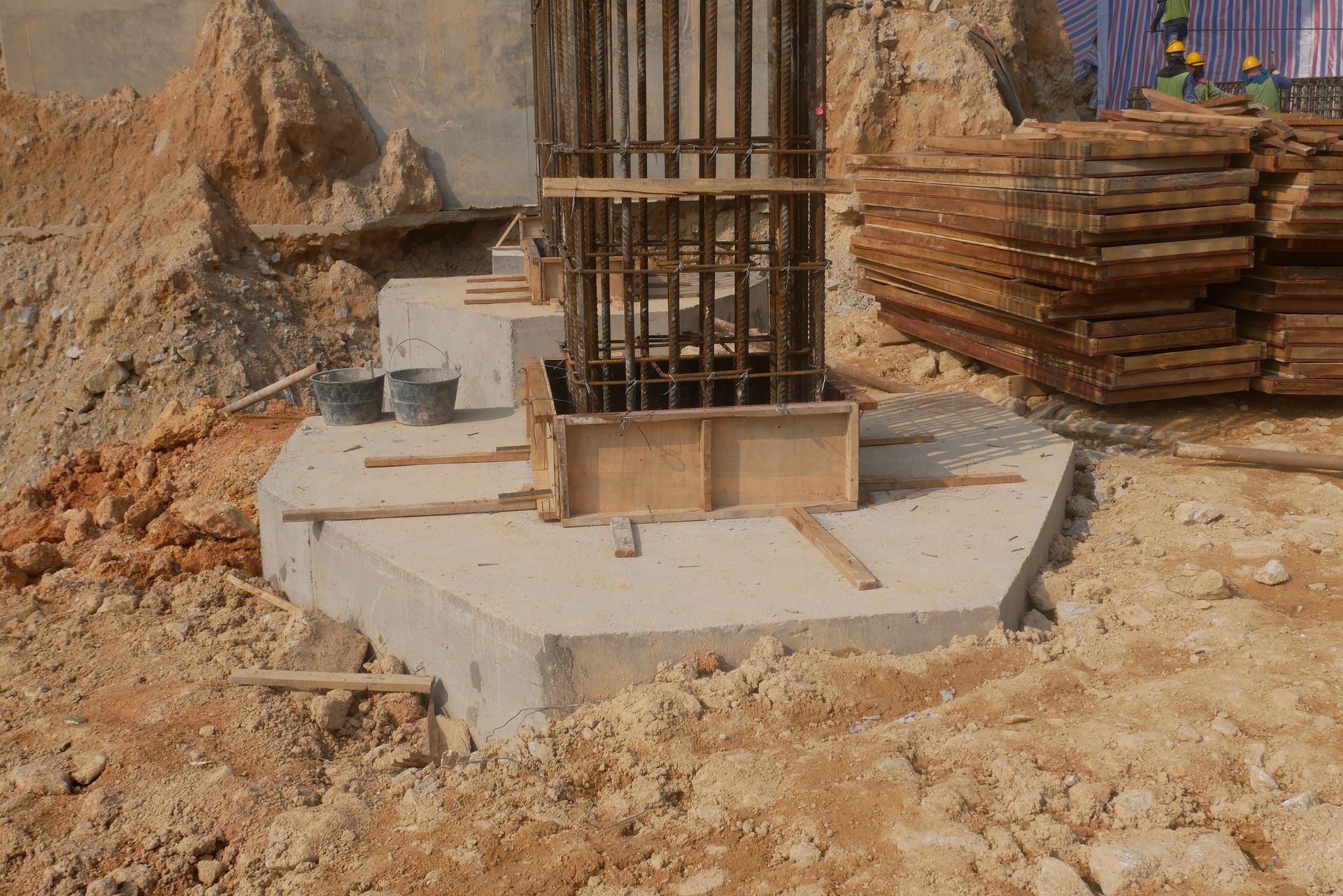 Concrete foundation under construction with rebar column and stacked wooden planks at a dirt site