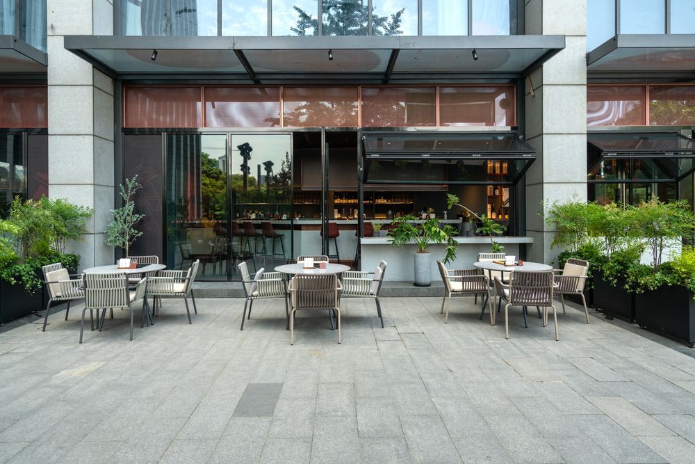 Outdoor café patio with metal tables and chairs in front of a modern glass storefront