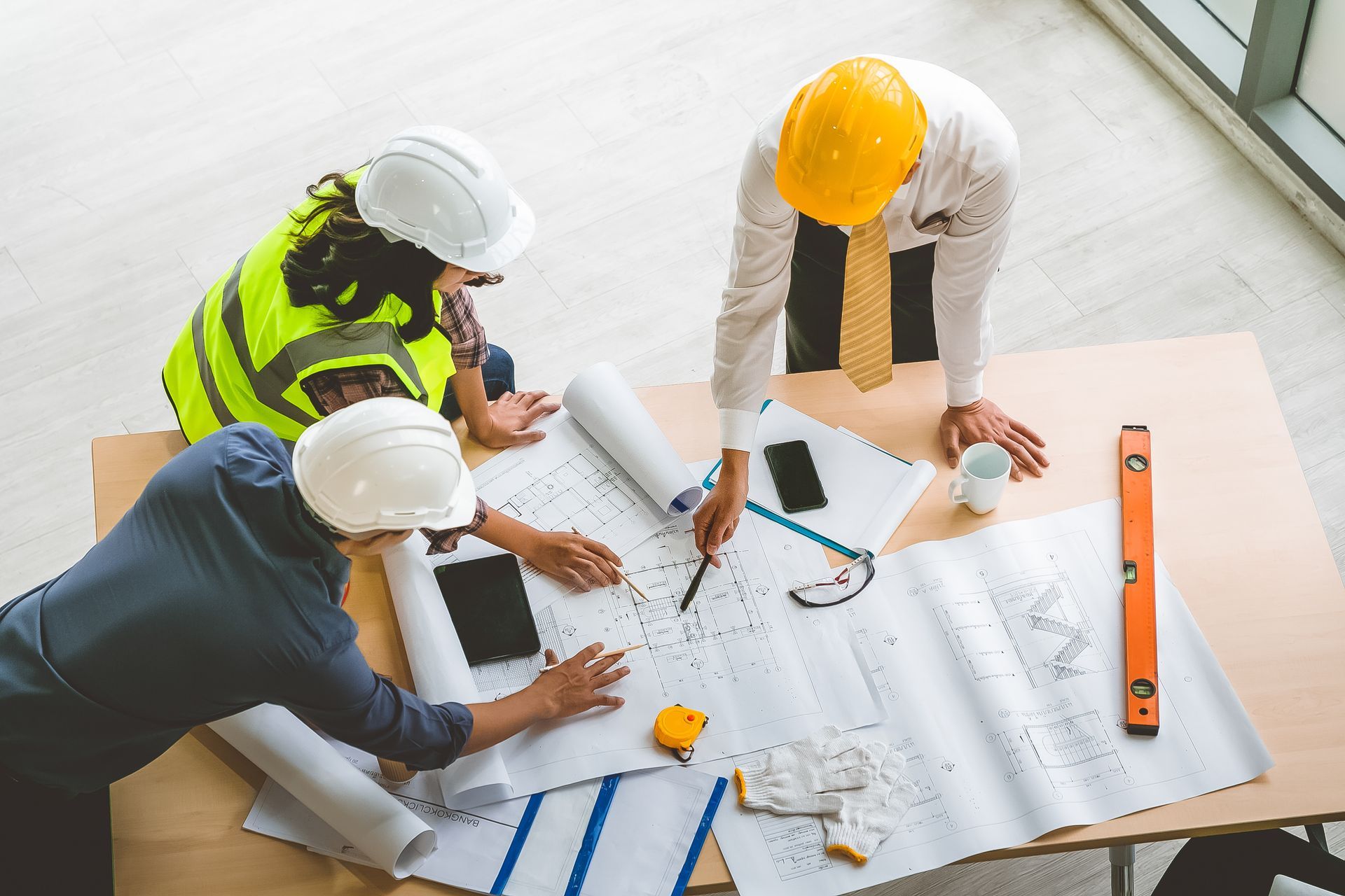Three workers in hard hats review blueprints at a bright construction site table