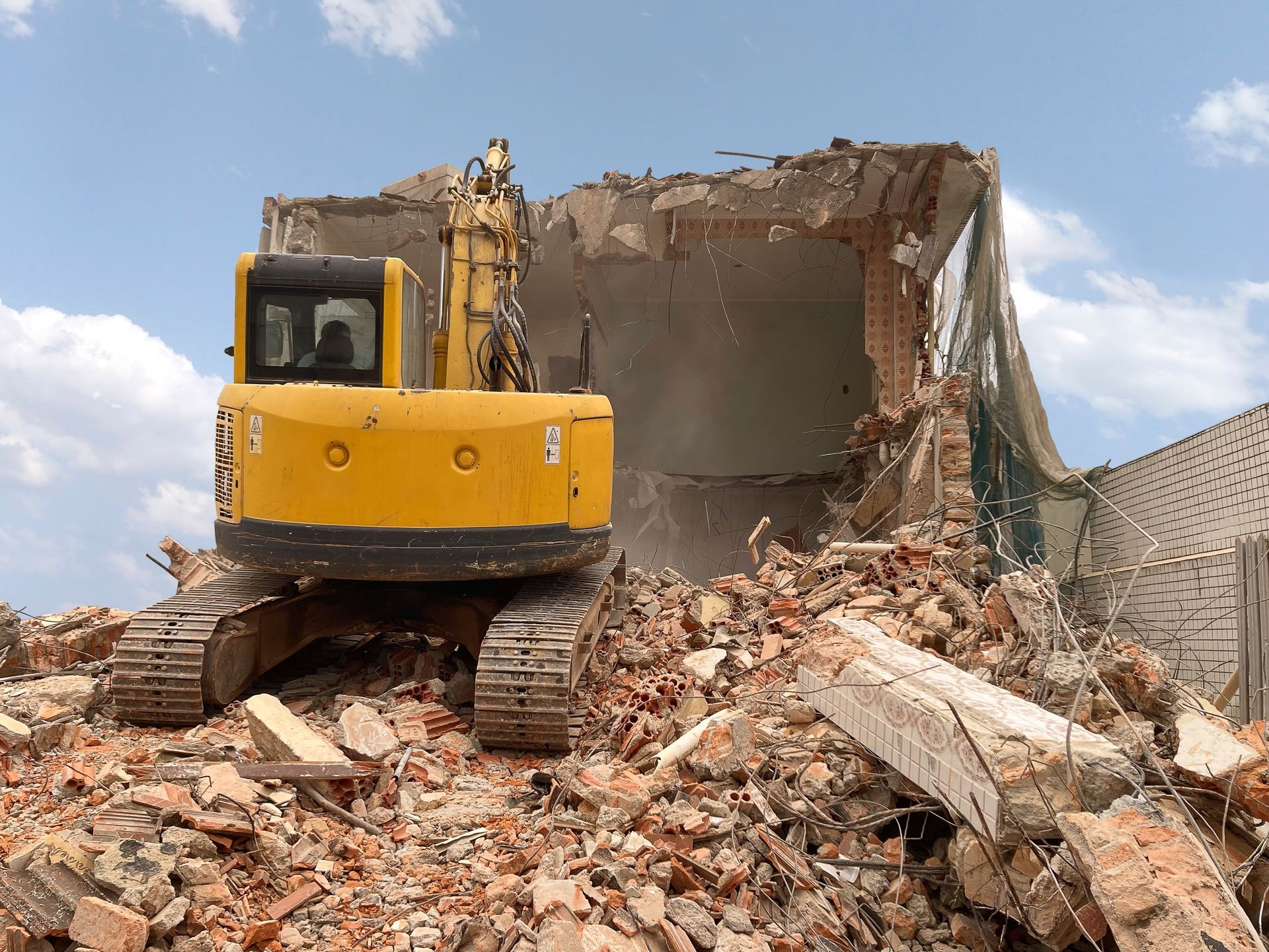 Yellow excavator demolishing a brick building amid rubble and dust