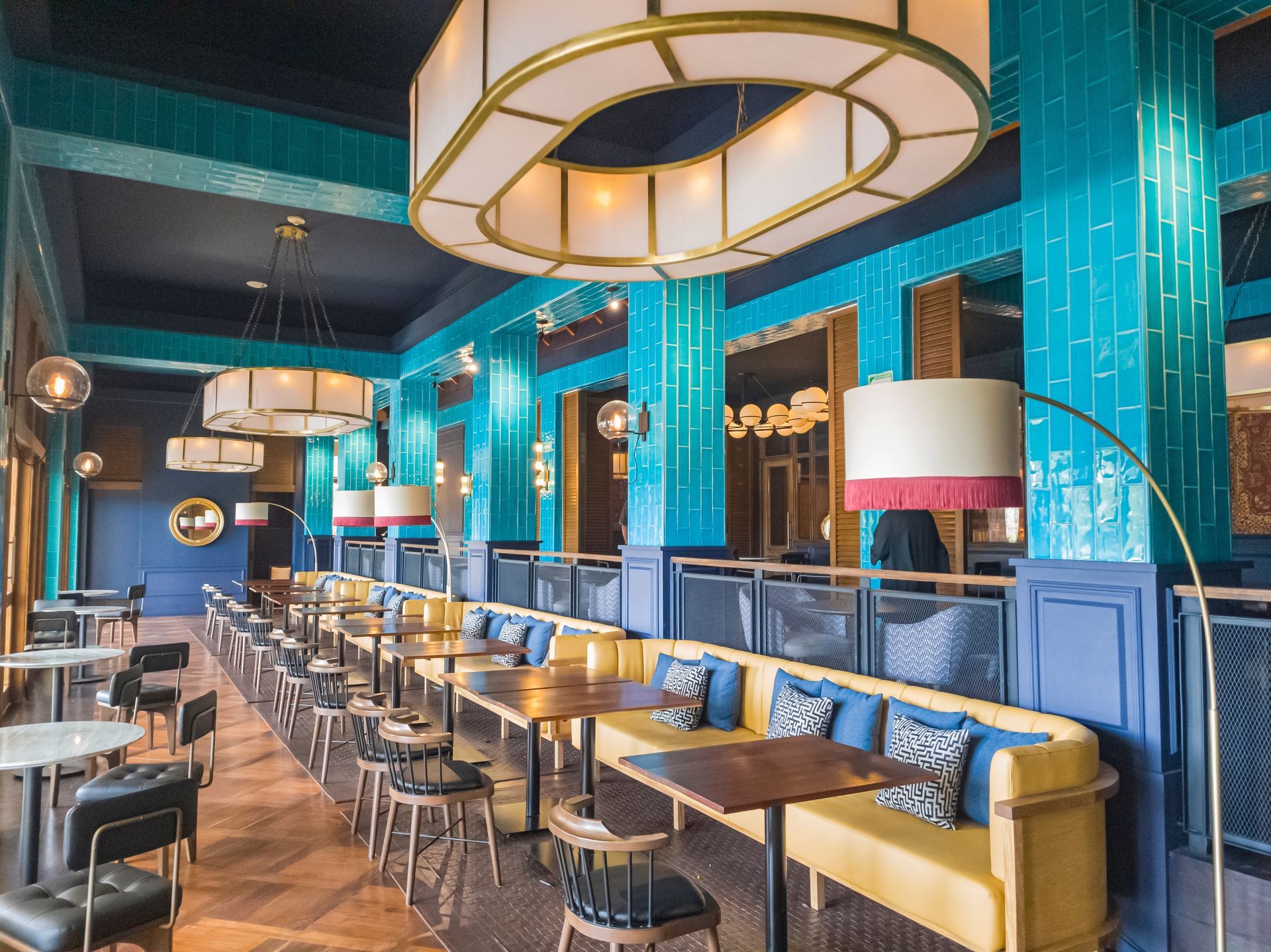 Turquoise restaurant interior with gold lighting, long tables, and blue booths along the wall