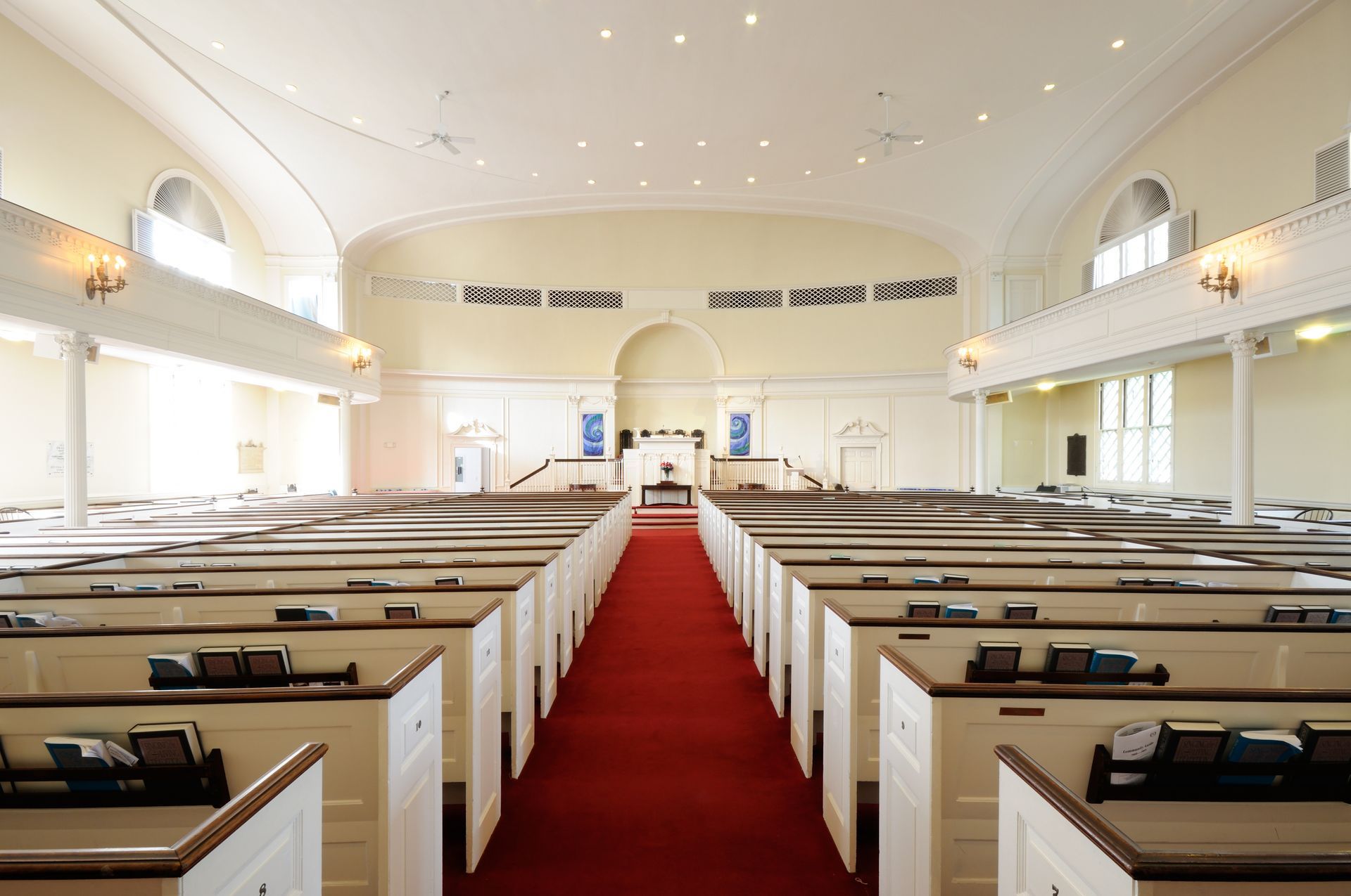 Empty church sanctuary with white pews and a red carpet aisle under a high arched ceiling