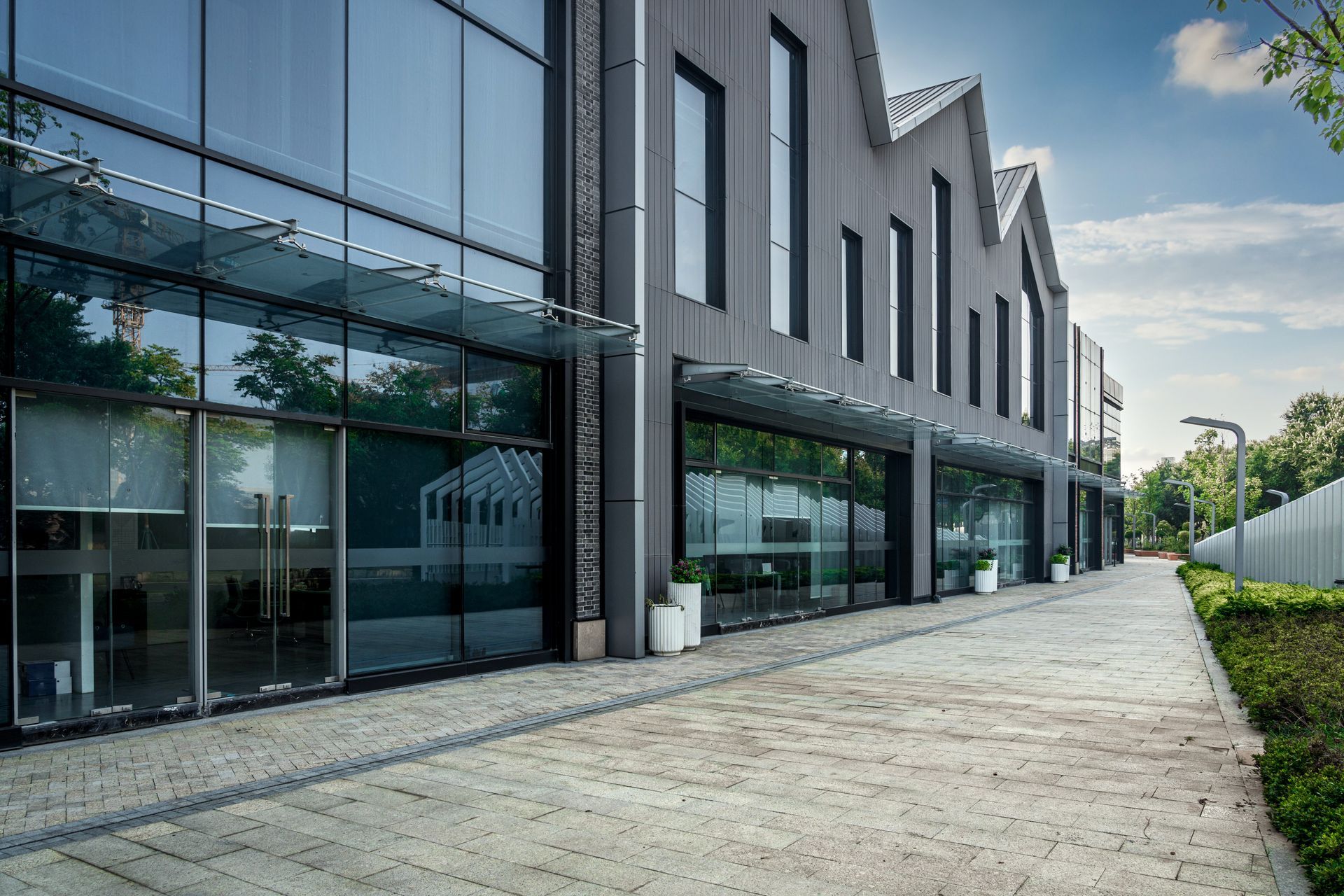 Modern industrial building with glass storefronts along a paved walkway under a blue sky