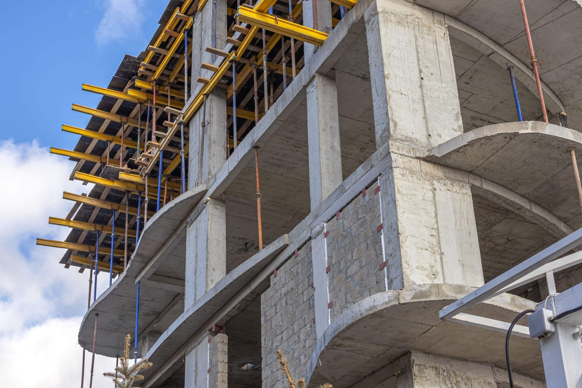 Partially built concrete building with scaffolding and yellow construction supports against a blue sky