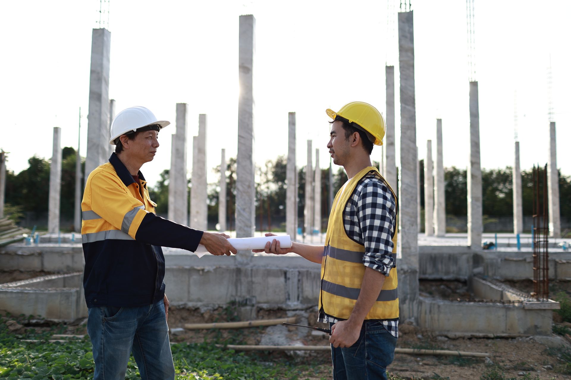 Two construction workers in hard hats shake hands at a building site.