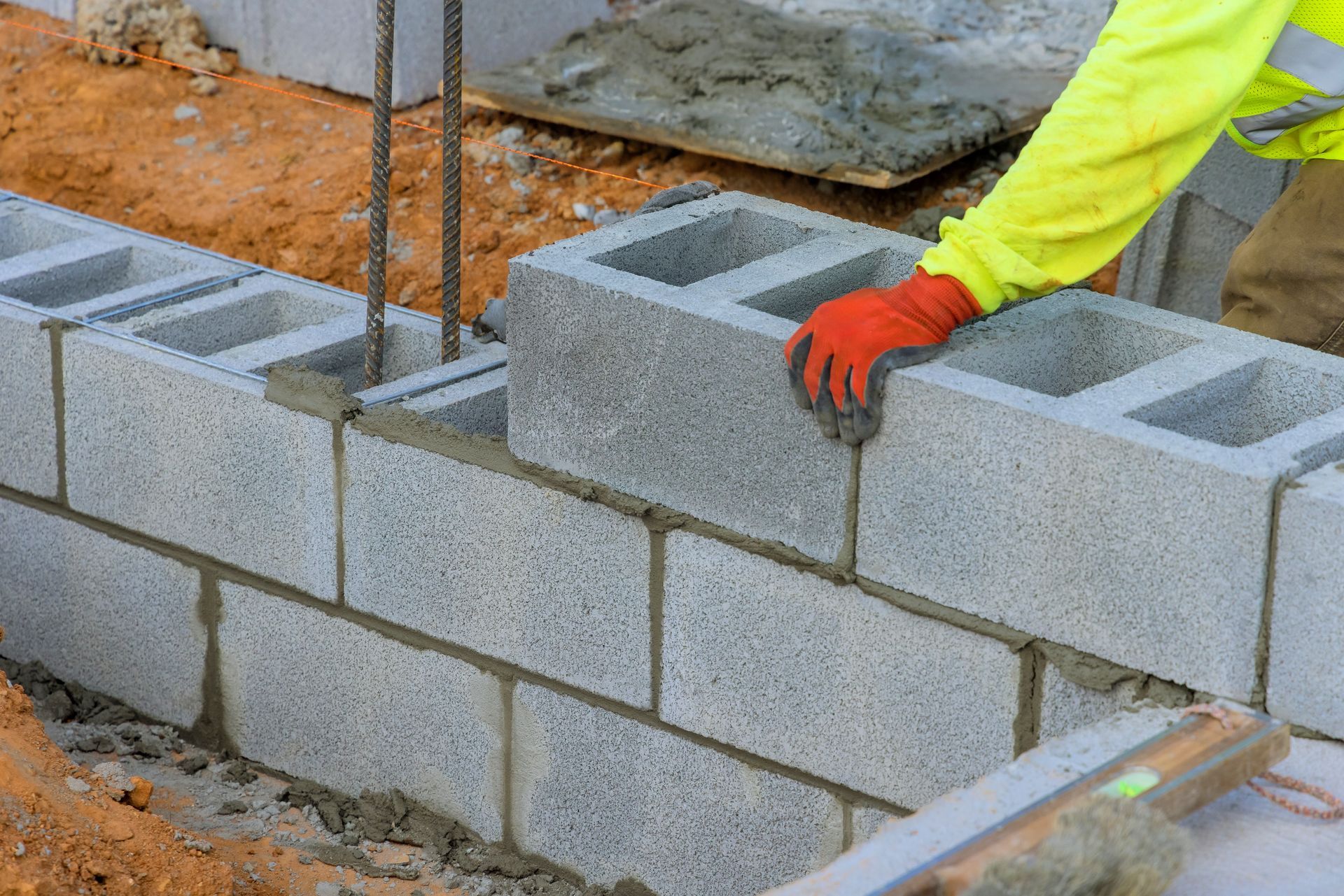 Worker laying cinder blocks at a construction site, wearing a neon yellow shirt and orange gloves