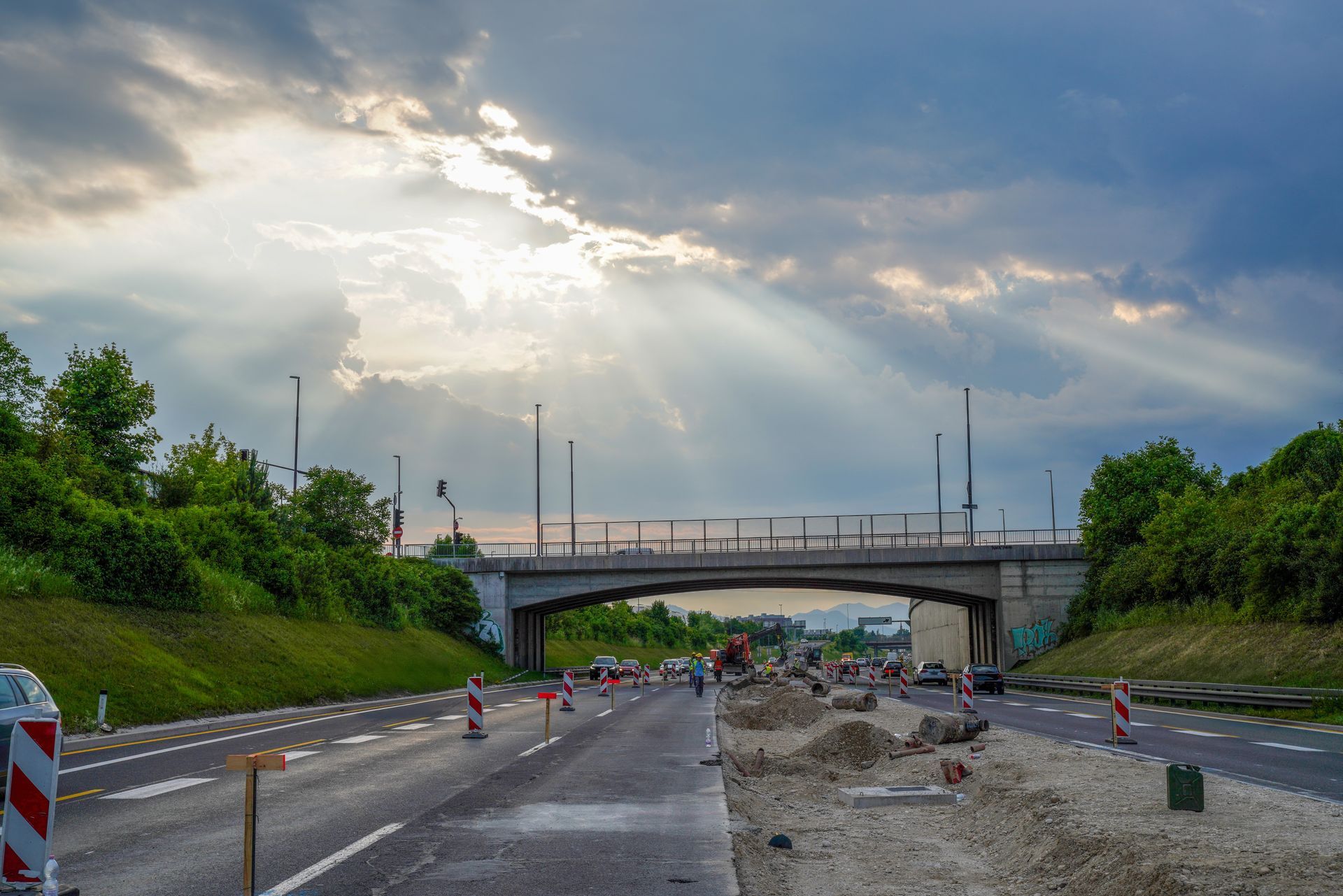 Road construction under a bridge with traffic cones and a cloudy sky
