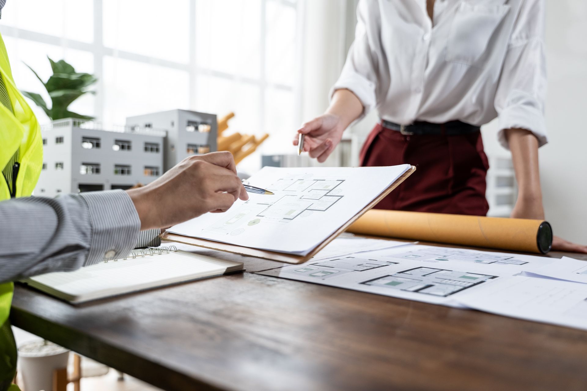 Two people reviewing floor plan drawings at a desk in a bright office