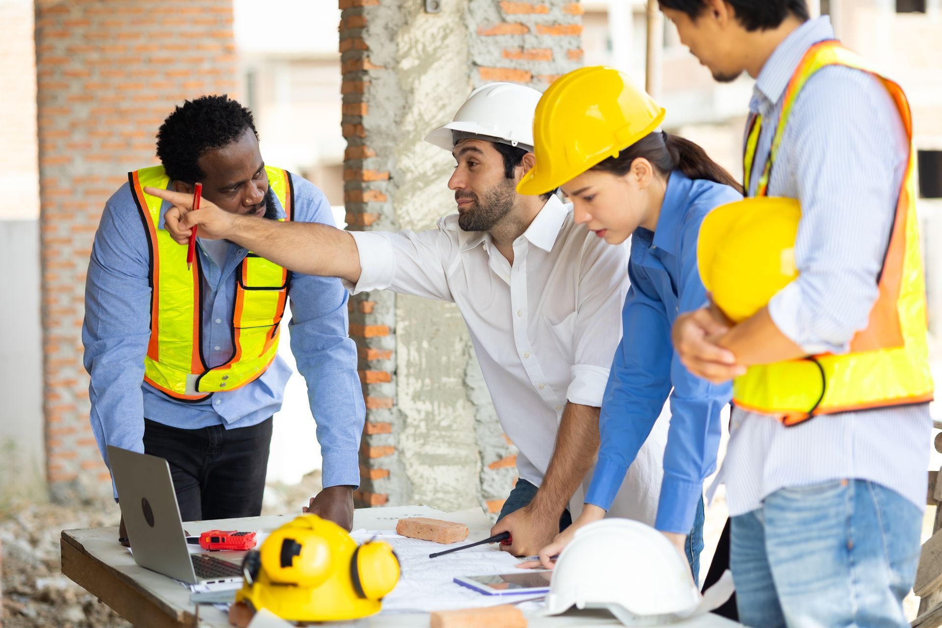 Construction team in safety vests and hard hats reviewing plans around a table in a renovation site