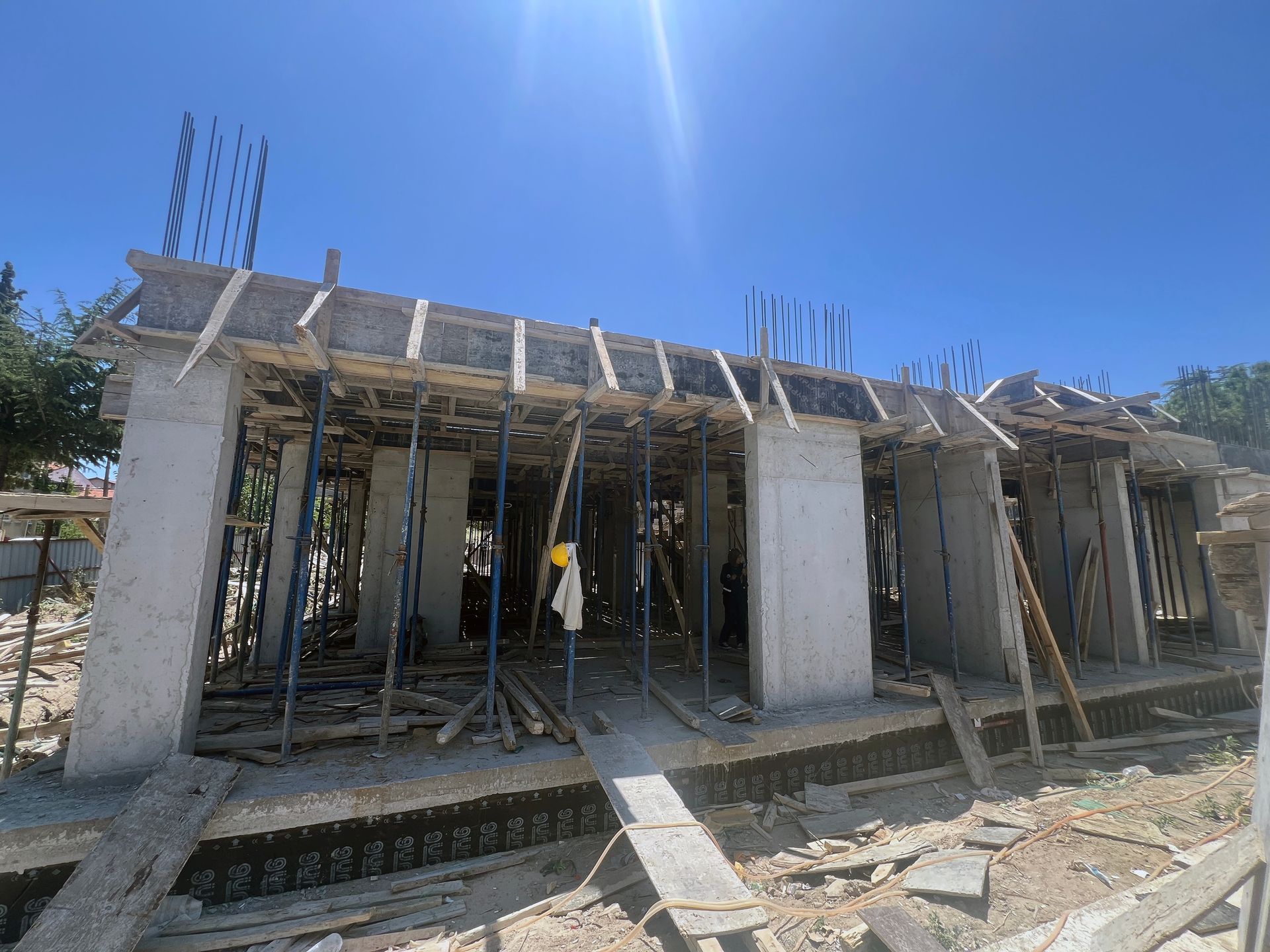 Partially built concrete structure with wooden scaffolding under a bright blue sky
