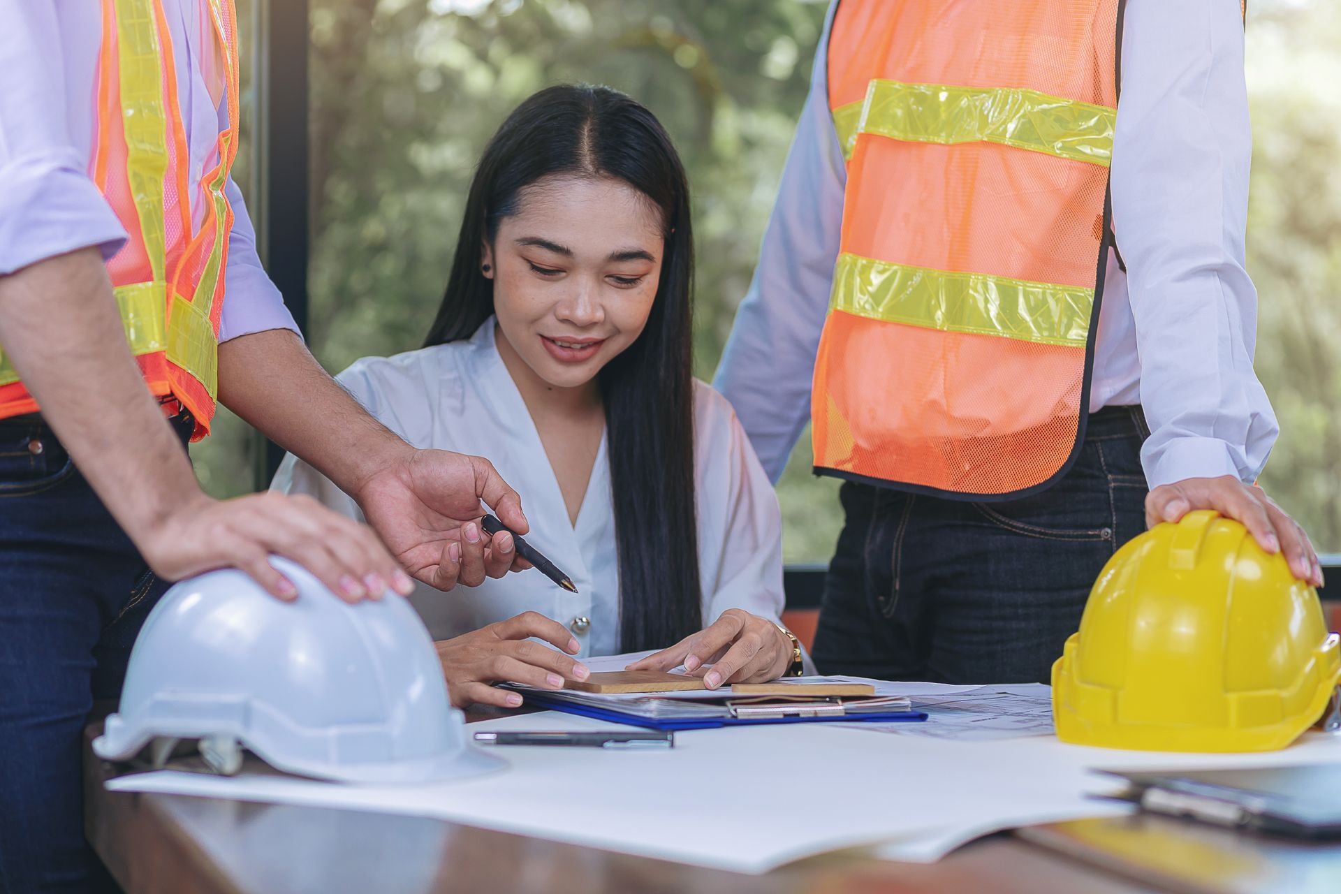 People reviewing plans at a construction site, with hard hats and safety vests on the table.