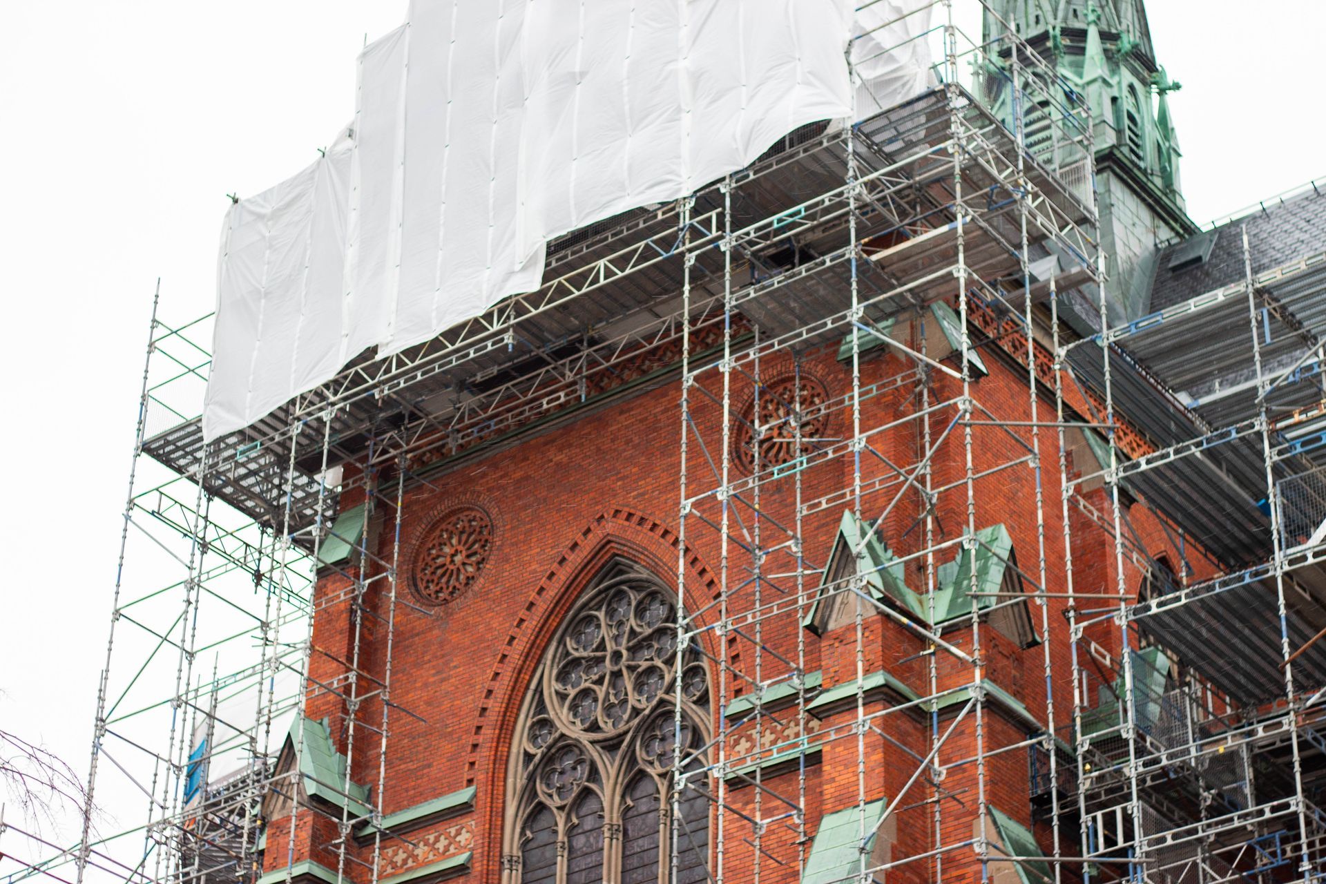 Red brick church tower under scaffolding, wrapped in white protective sheeting during restoration.