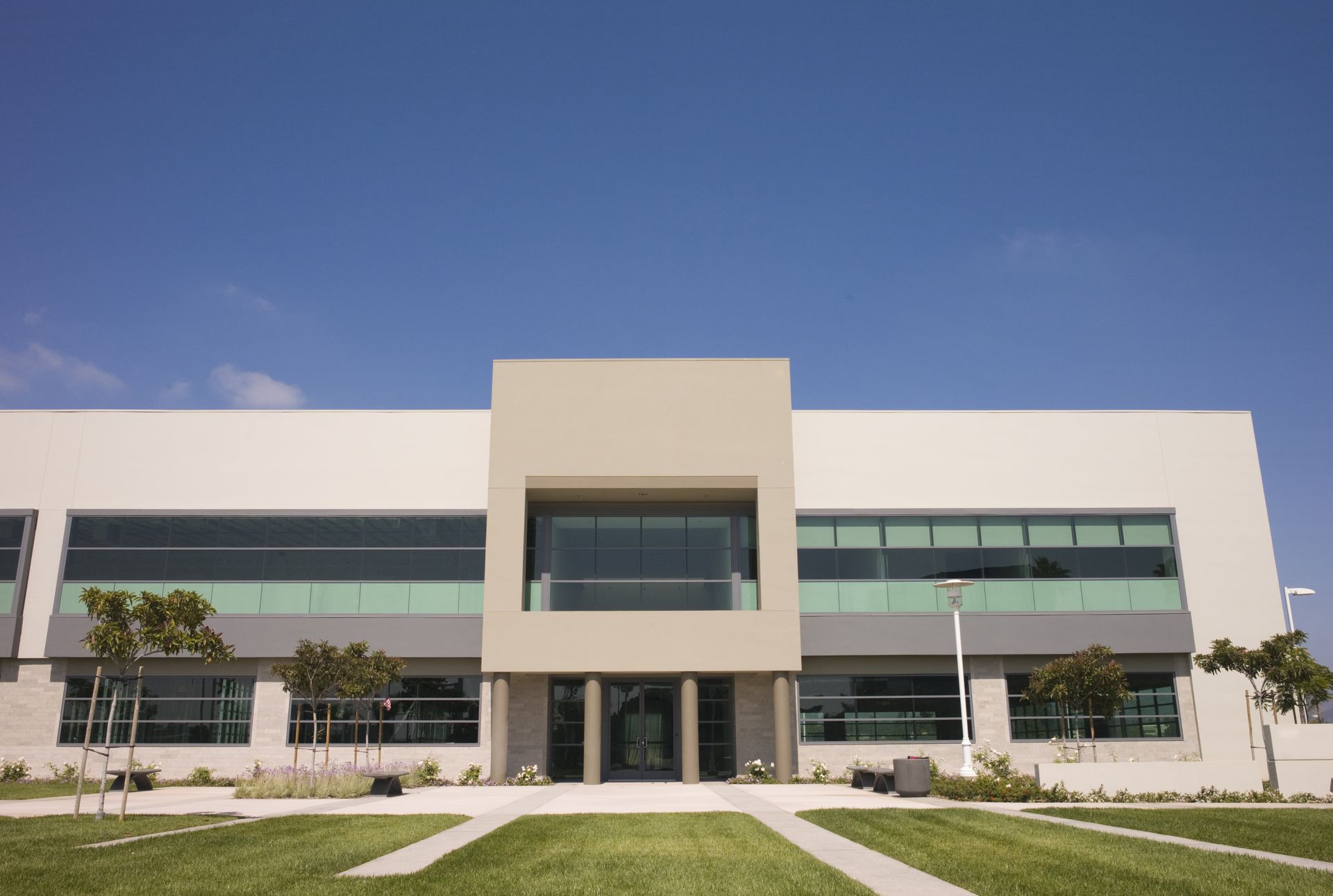 Modern hospital building with a beige central entrance, glass windows, and a manicured lawn under a clear blue sky