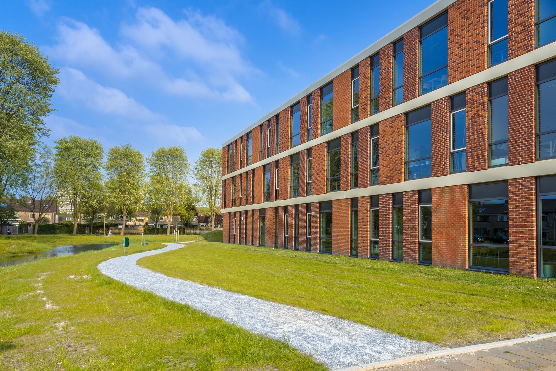 Modern brick building beside a curving white path on a green lawn under a blue sky