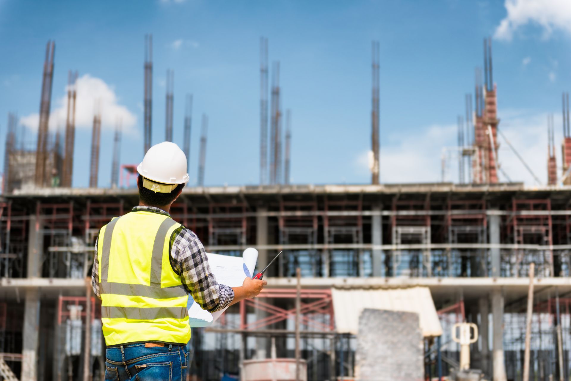 Two construction workers in hard hats review plans at a building site.