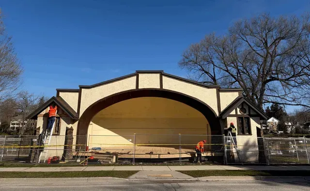 Outdoor stage with cream and brown arch, flanked by stairs, under a clear blue sky.