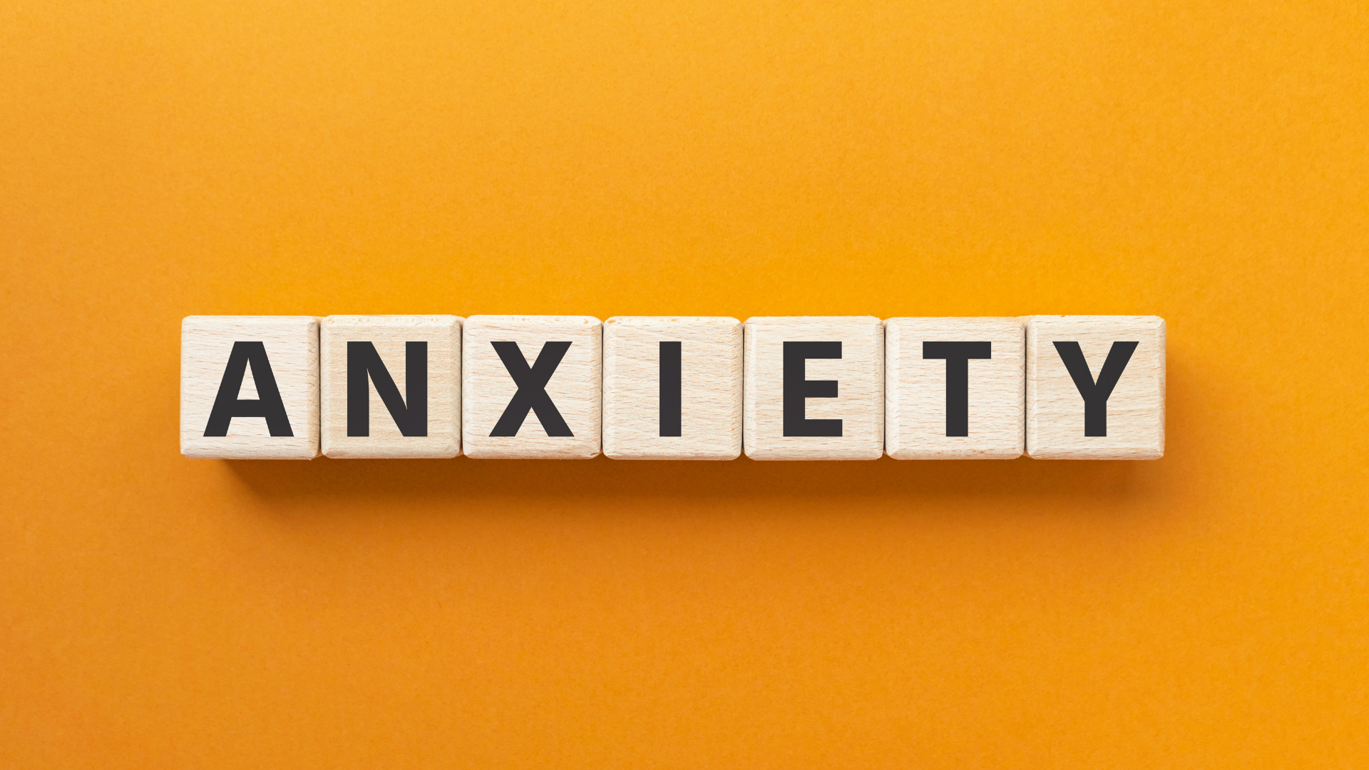 Scrabble tiles spelling “ANXIETY” on a bright orange background