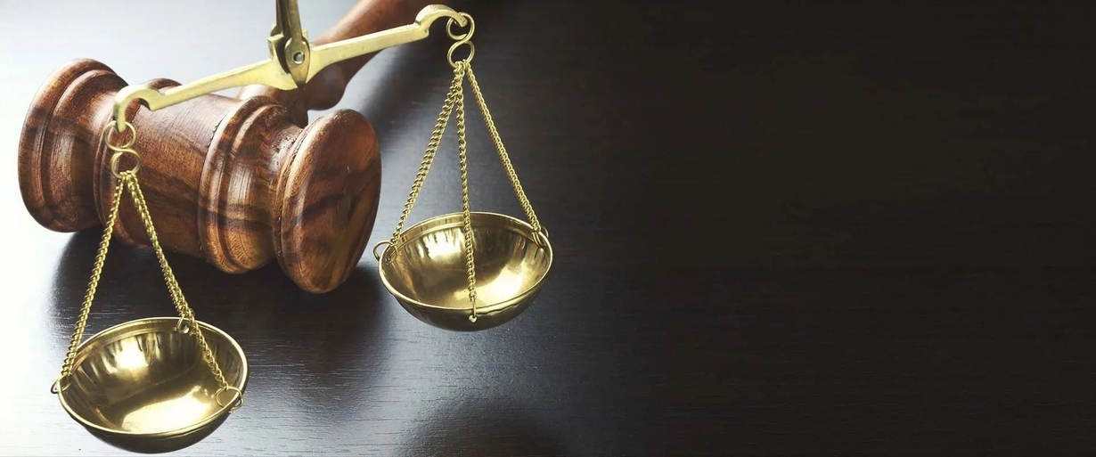 A wooden judge's gavel rests beside a pair of brass scales of justice on a dark surface.