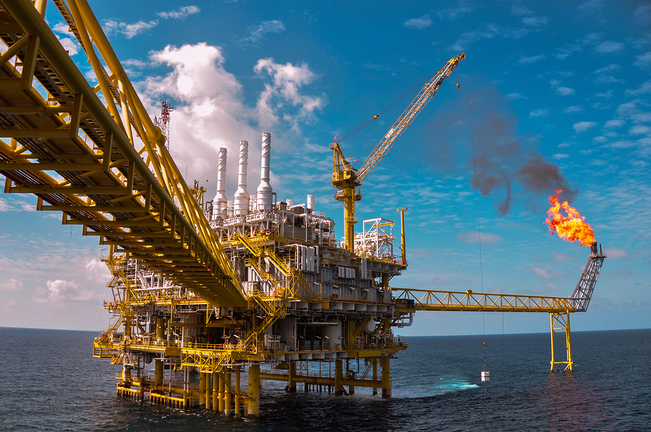 An oil rig in the middle of the ocean with flames coming out of it.