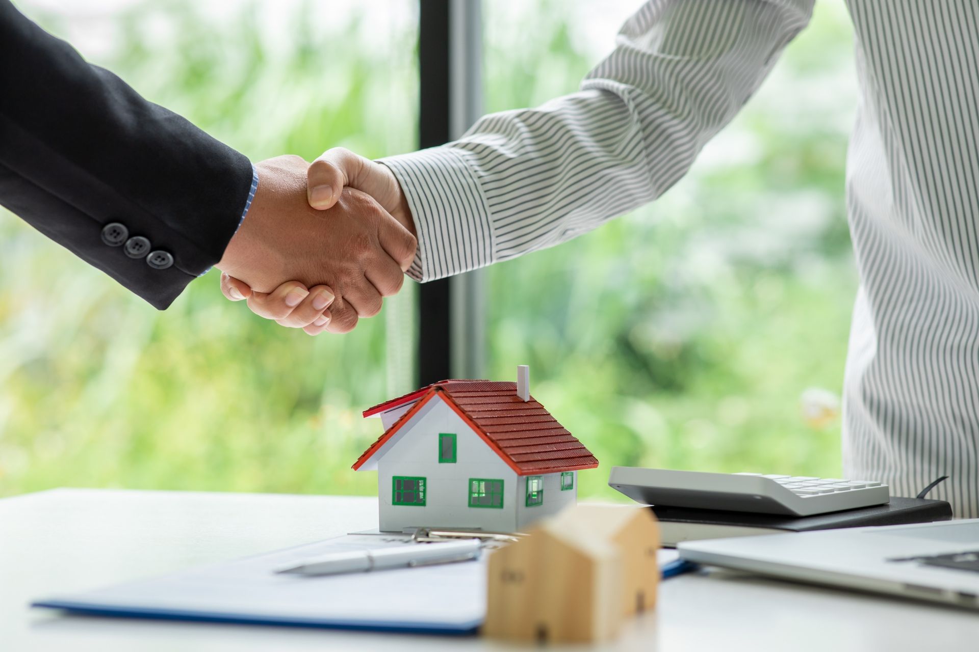 Business handshake over desk with small house model and paperwork