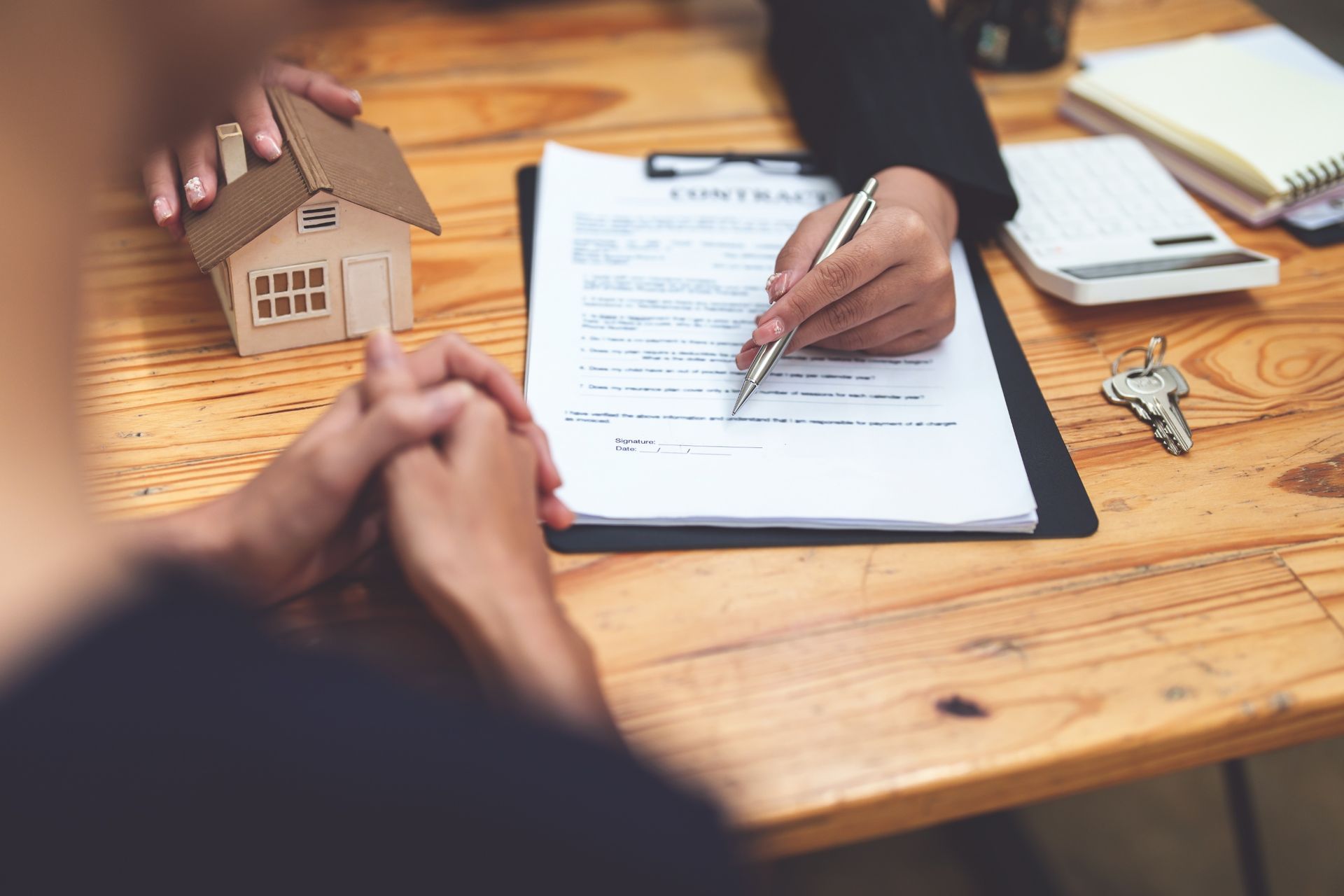 Hands completing a loan application at a wooden table with a small house model and keys nearby