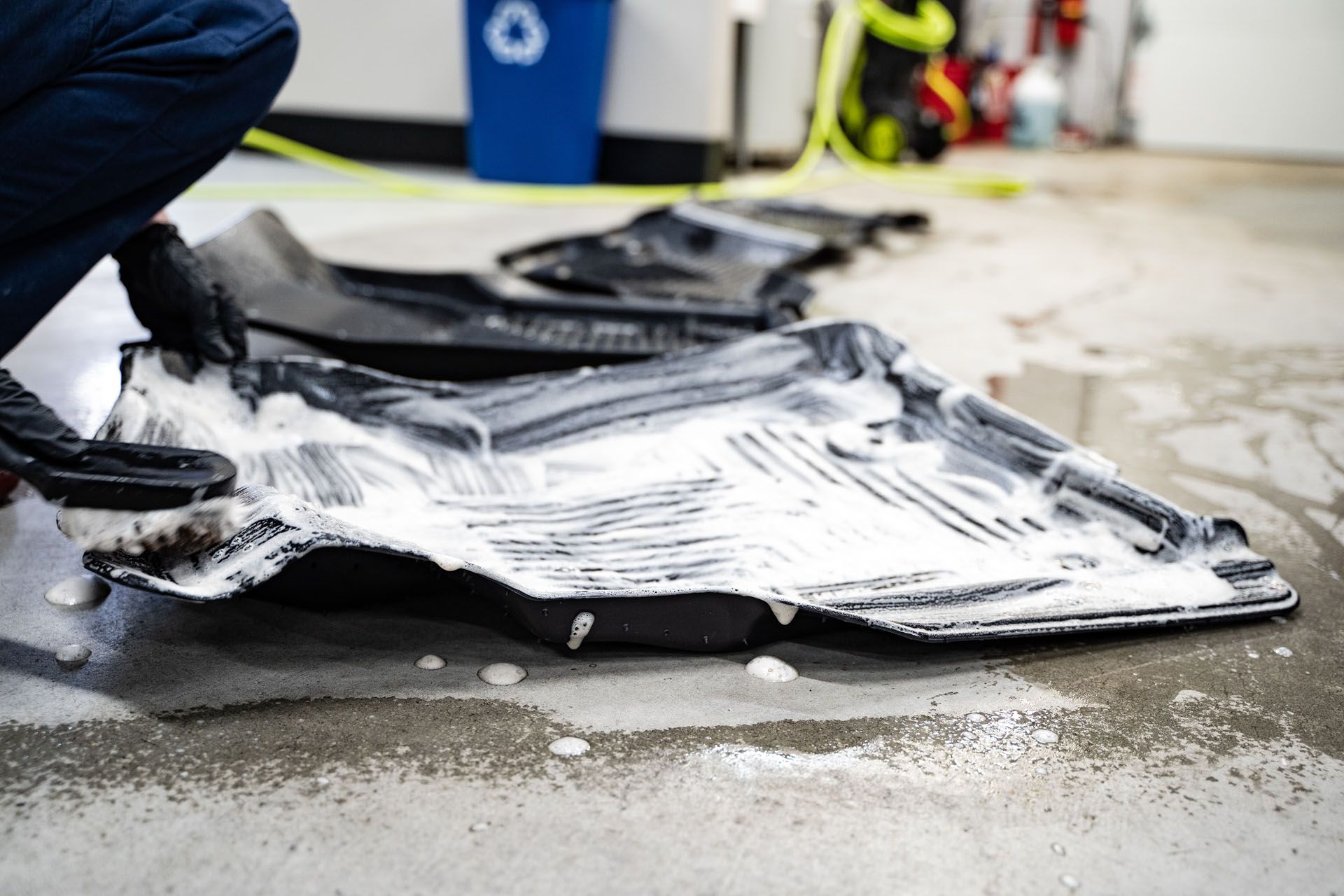 A person is kneeling down to clean a rubber mat on the floor.