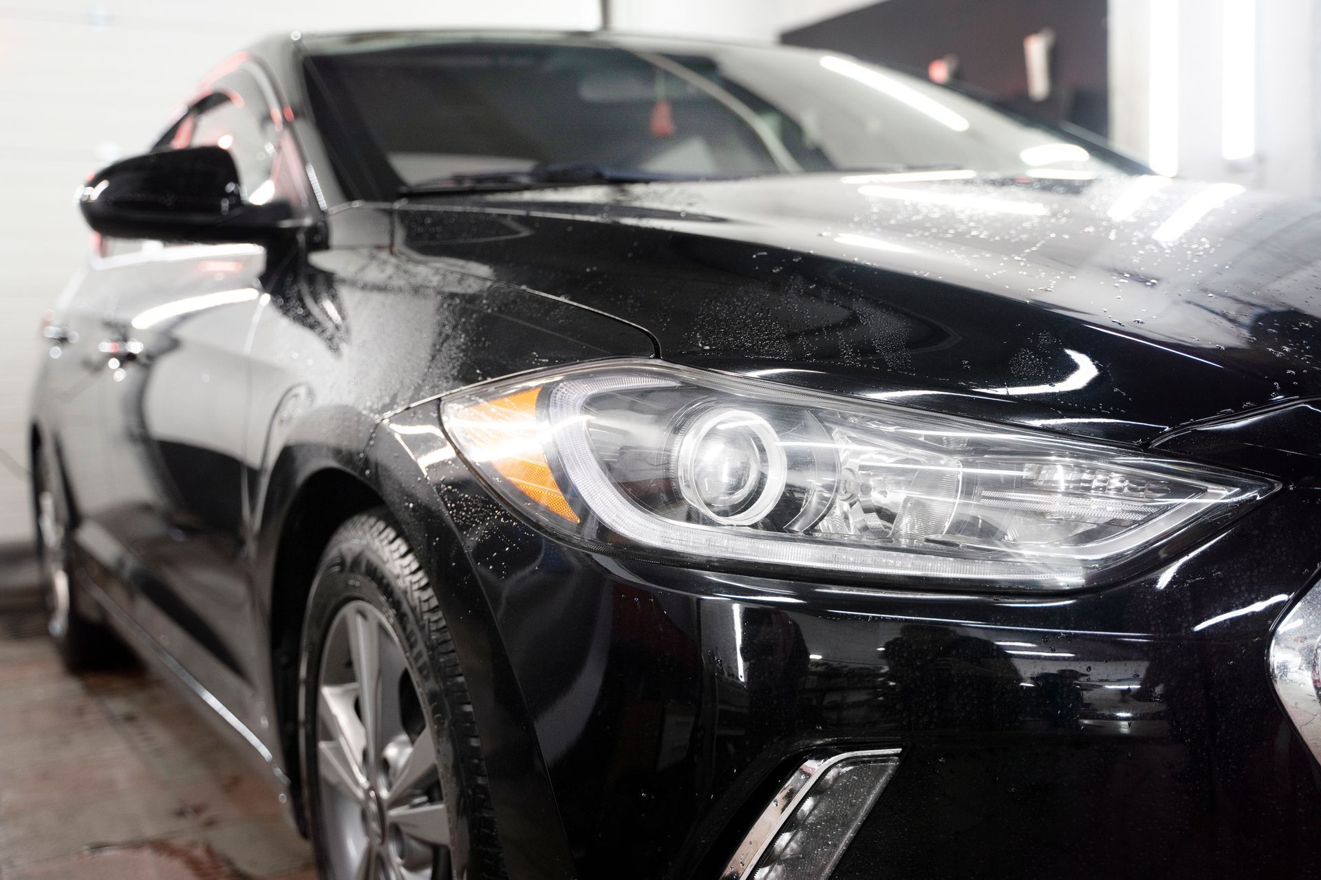 A black car is parked in a garage next to a wall.