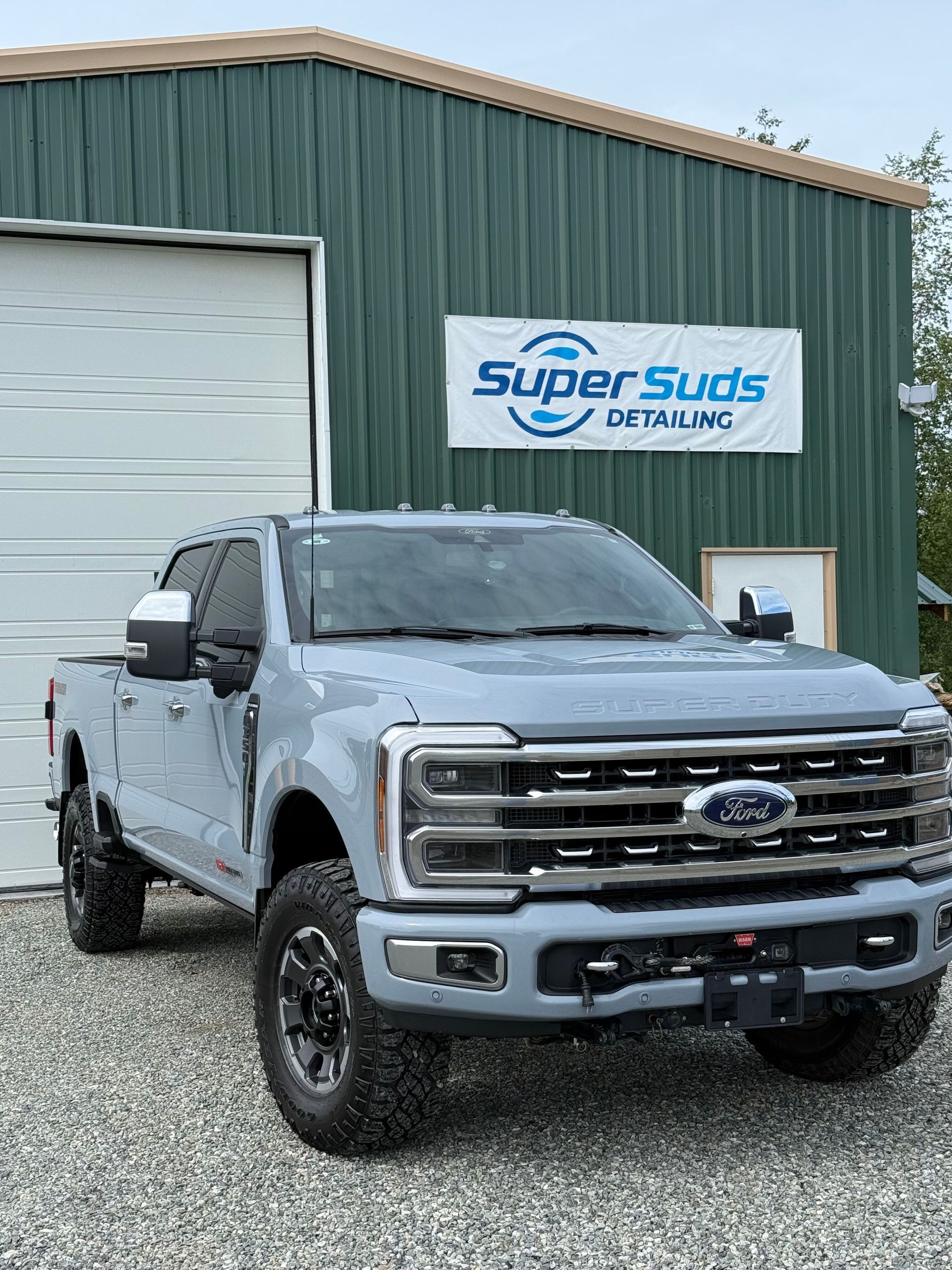 A gray ford truck is parked in front of a green building.