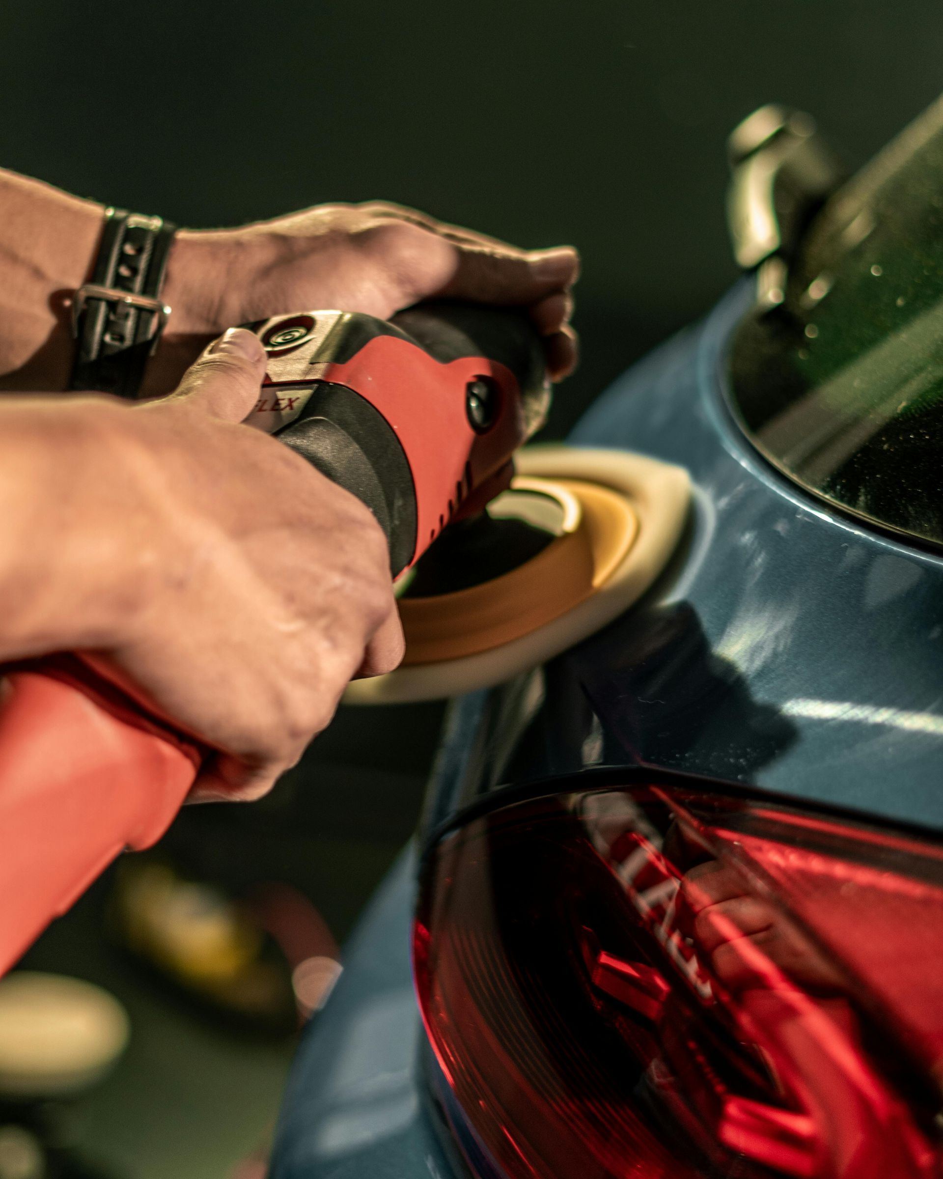 A person is polishing the back of a blue car