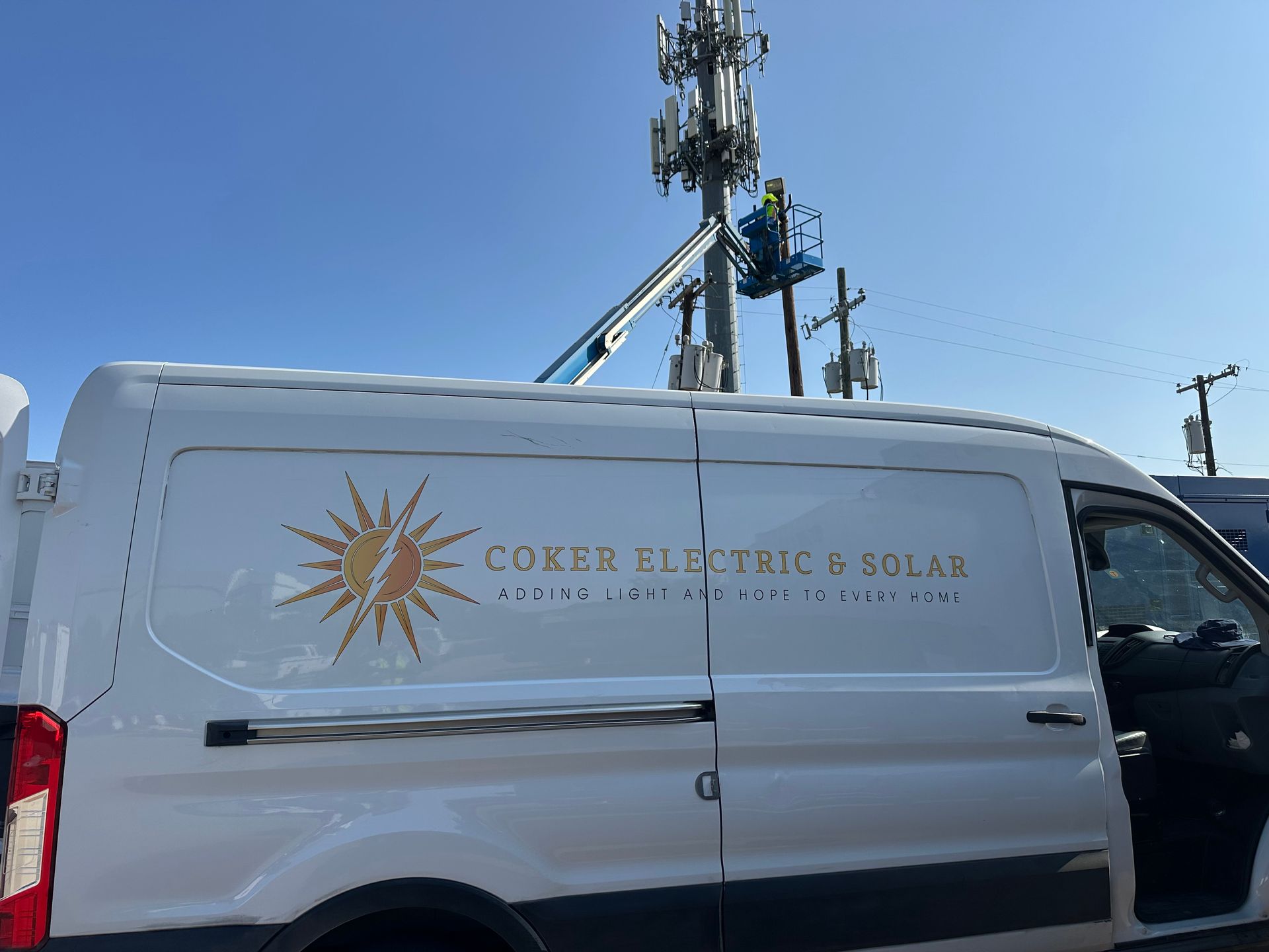 White service van with “Coxen Electric & Solar” logo parked near utility poles and cell towers under a blue sky
