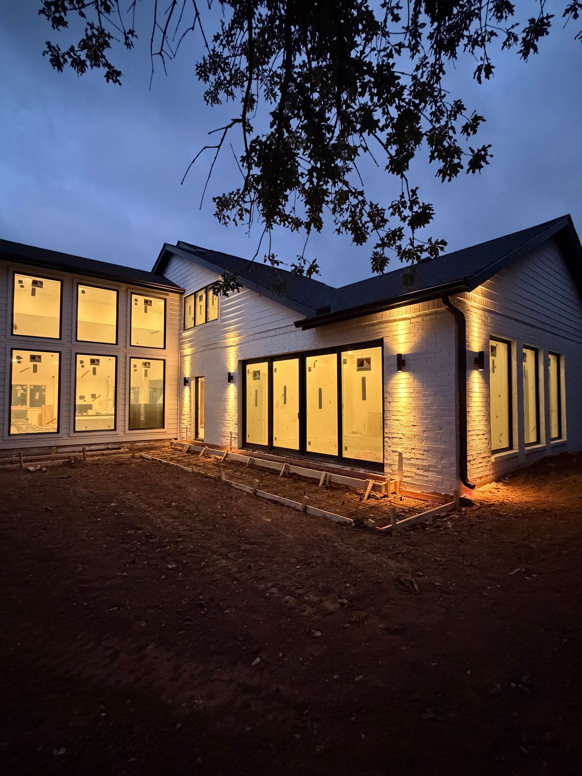 Modern house exterior at dusk with warm interior lights and lit porch under a dark blue sky
