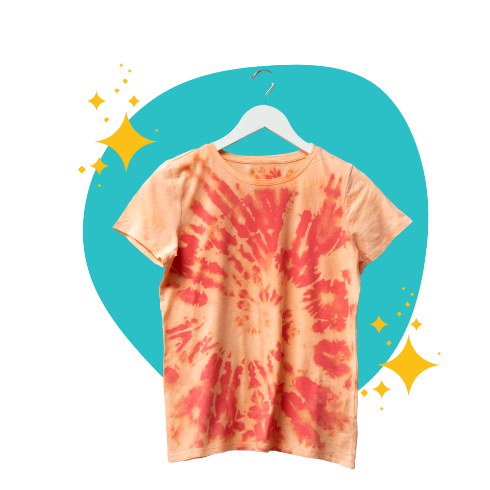 T-shirt color pesca tie-dye con dettagli glitterati color verde acqua e oro, appesa a una gruccia.