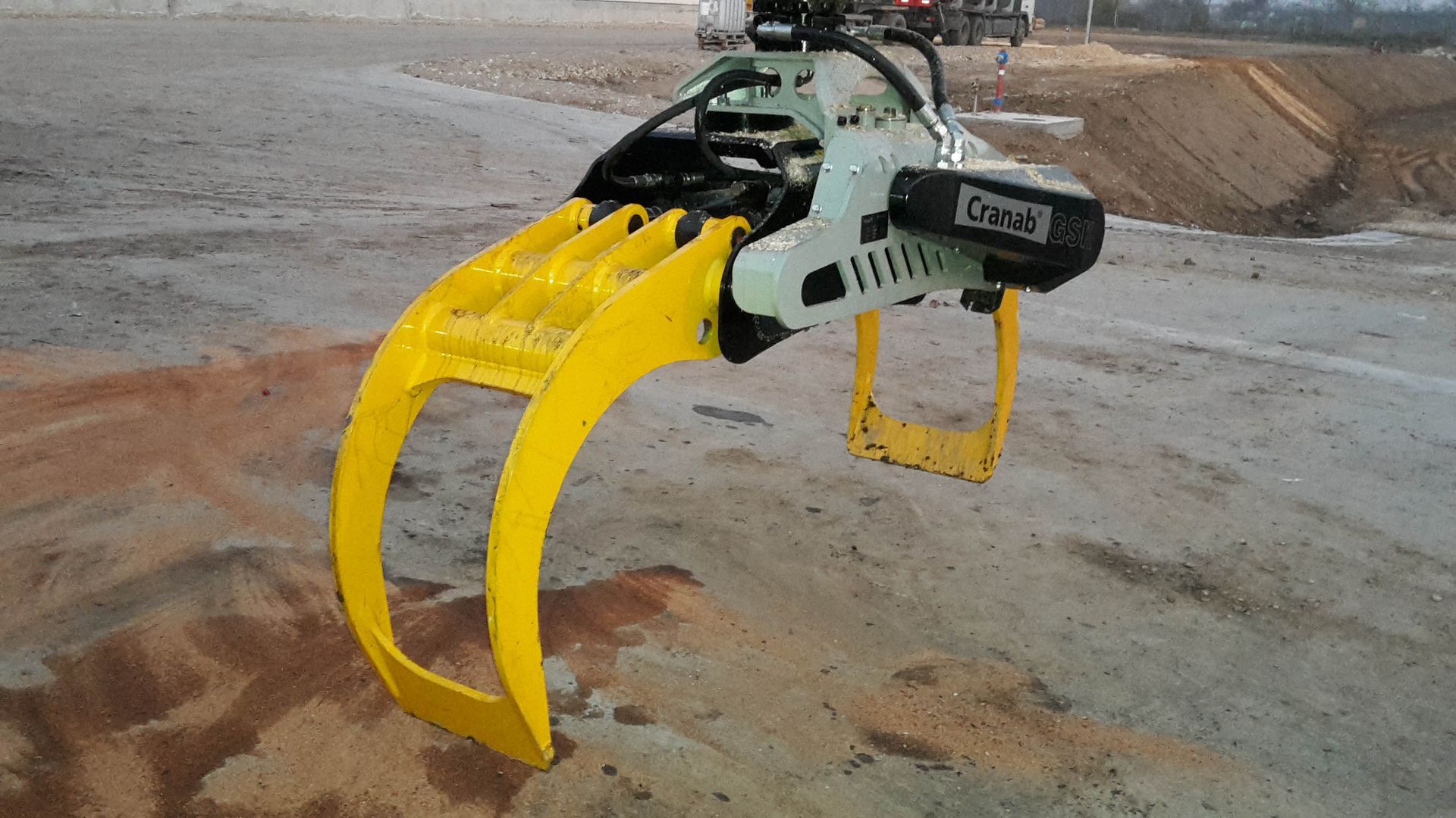 Un attacco a pinza giallo su un macchinario pesante, sollevato sopra un mucchio di terra.