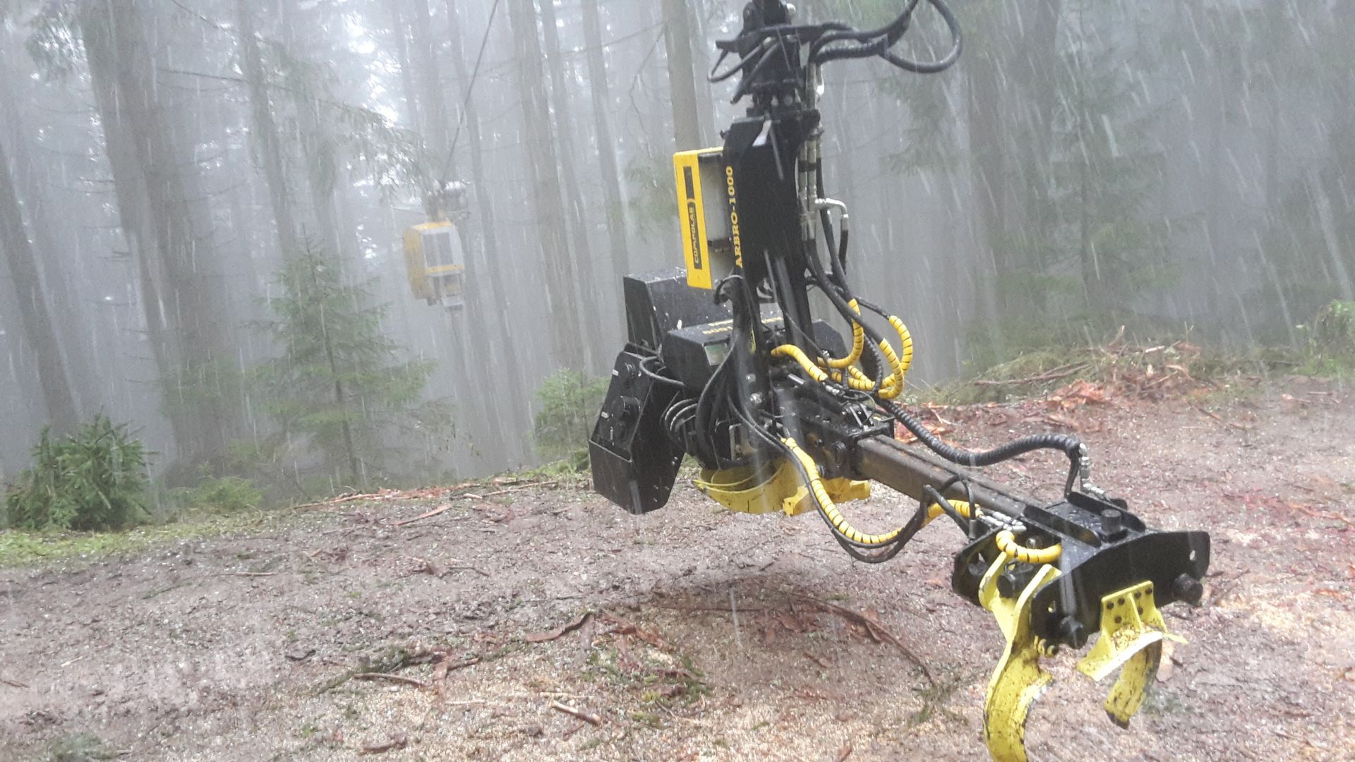 Un macchinario per il disboscamento giallo e nero in una foresta, con un altro macchinario sullo sfondo.