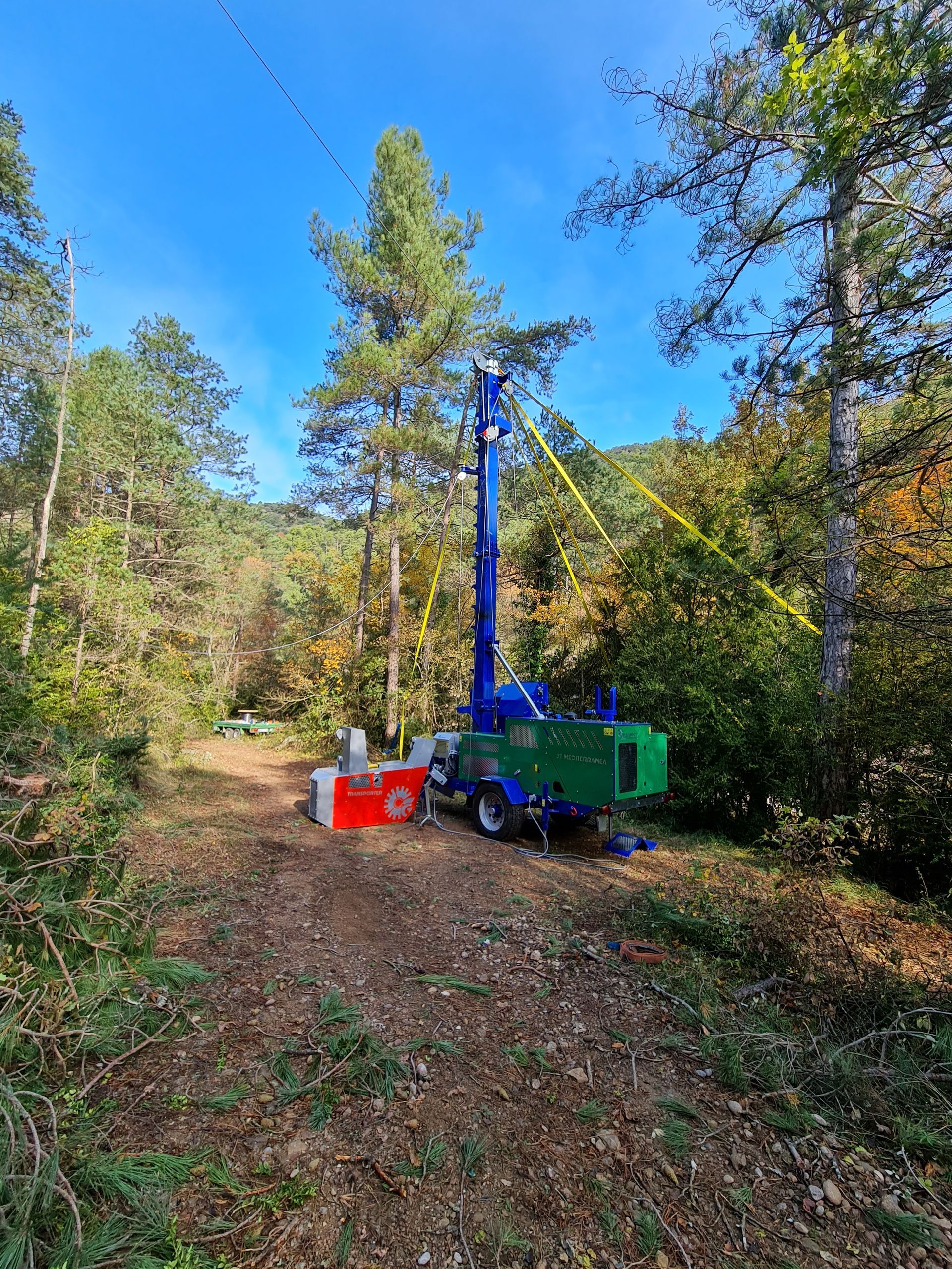 Una macchina perforatrice blu e verde in una radura della foresta, intenta a perforare un albero.