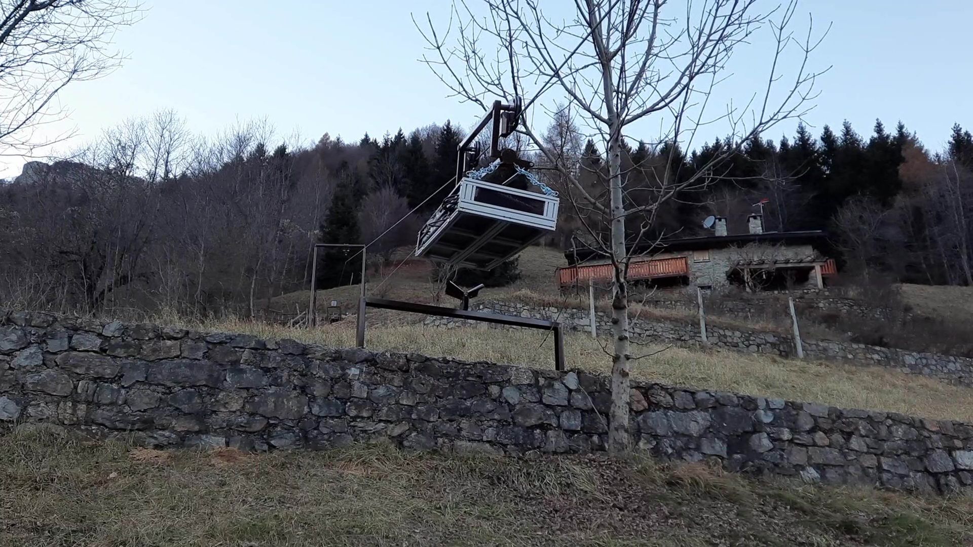 Una seggiovia incastrata in un albero vicino a un muro di pietra e a una collina con un edificio sullo sfondo.