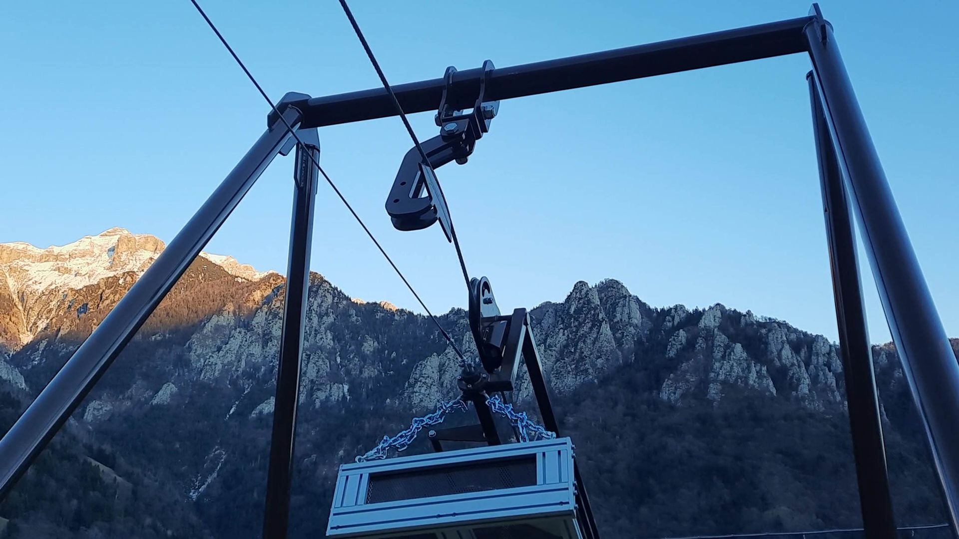 Un sistema di funivia con una cabina sospesa a un cavo sullo sfondo di montagne.