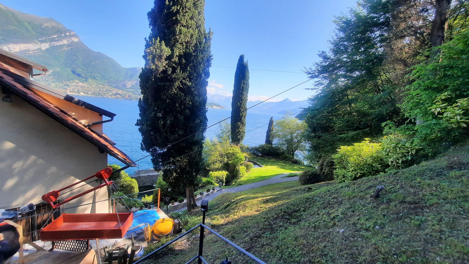 Casa con vista su un lago, con montagne in lontananza, alberi alti e vegetazione lussureggiante.
