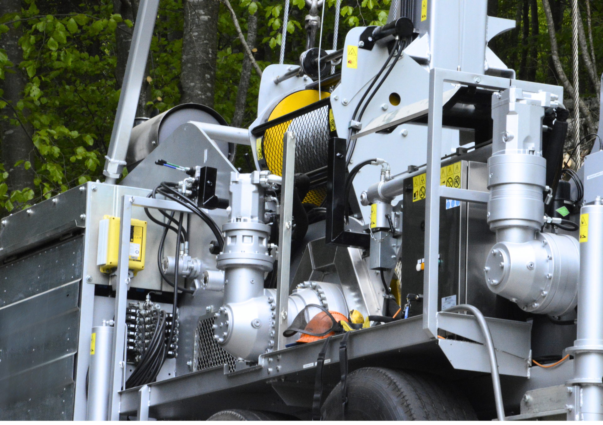 Cassone di camion con macchinari, caratterizzato da componenti argentati, un cilindro giallo e avvertenze di sicurezza.