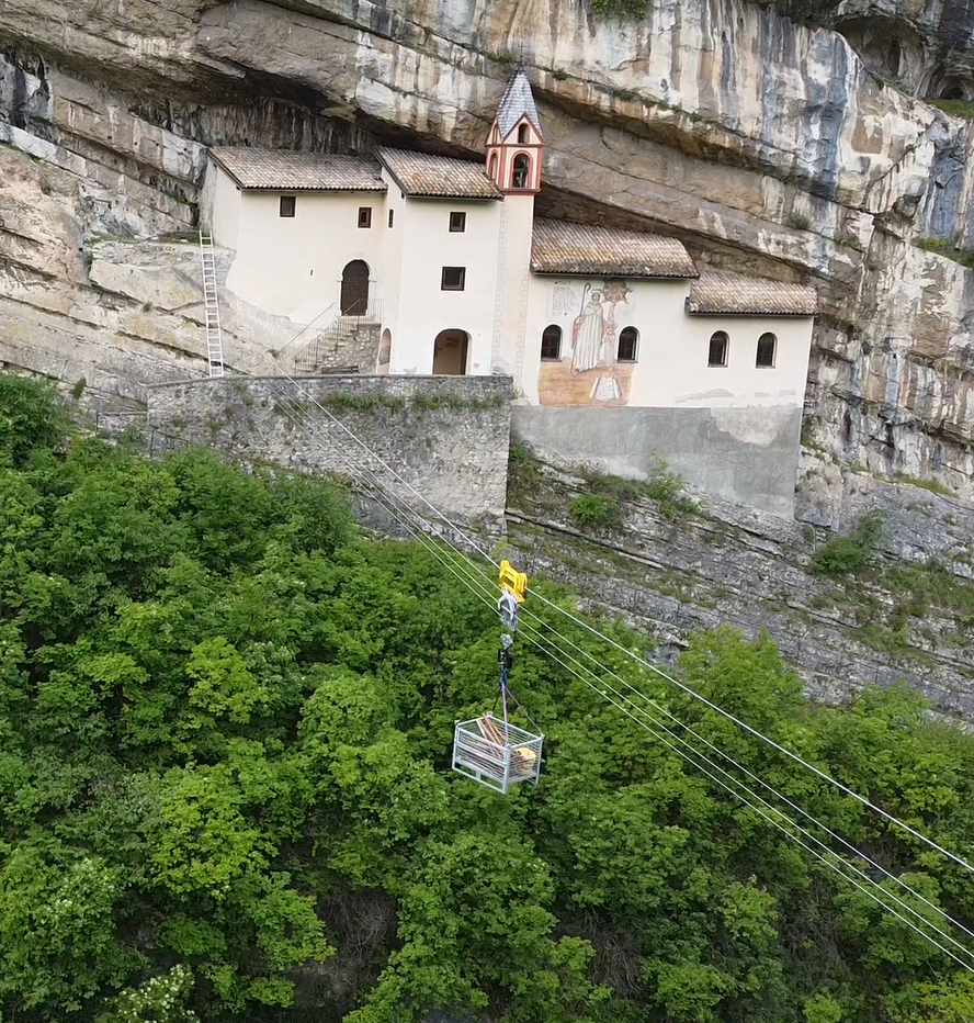 Chiesa costruita sulla parete di una scogliera, con una funivia che trasporta i rifornimenti tra gli alberi.