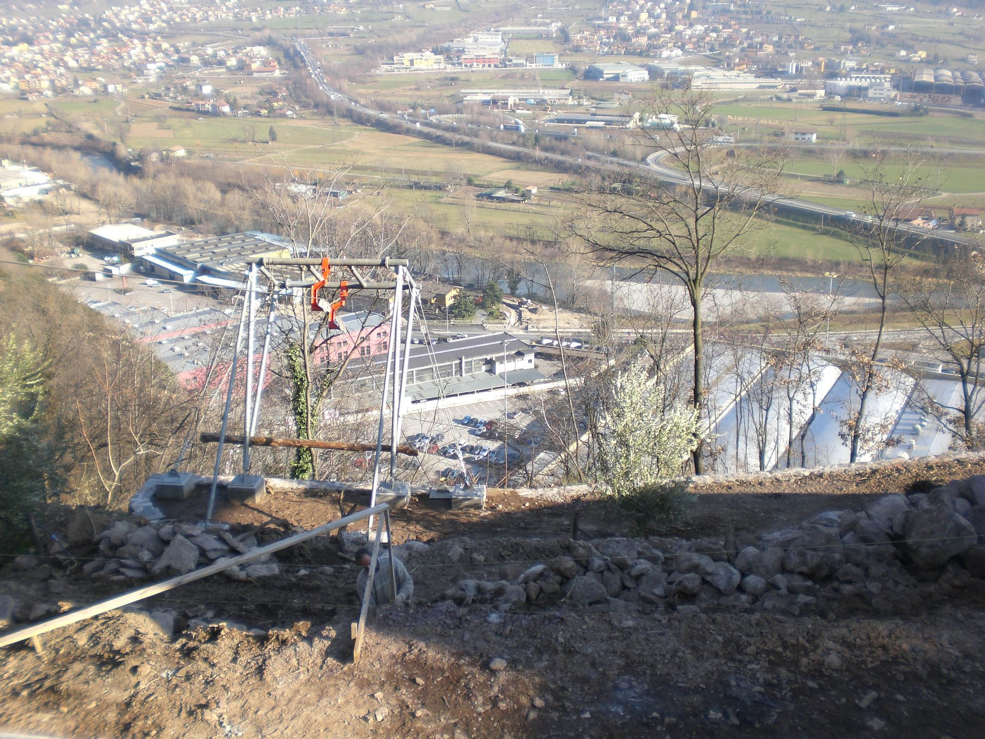 Ripresa dall'alto: una persona lavora su una struttura metallica, con vista su una città, un fiume e una strada.
