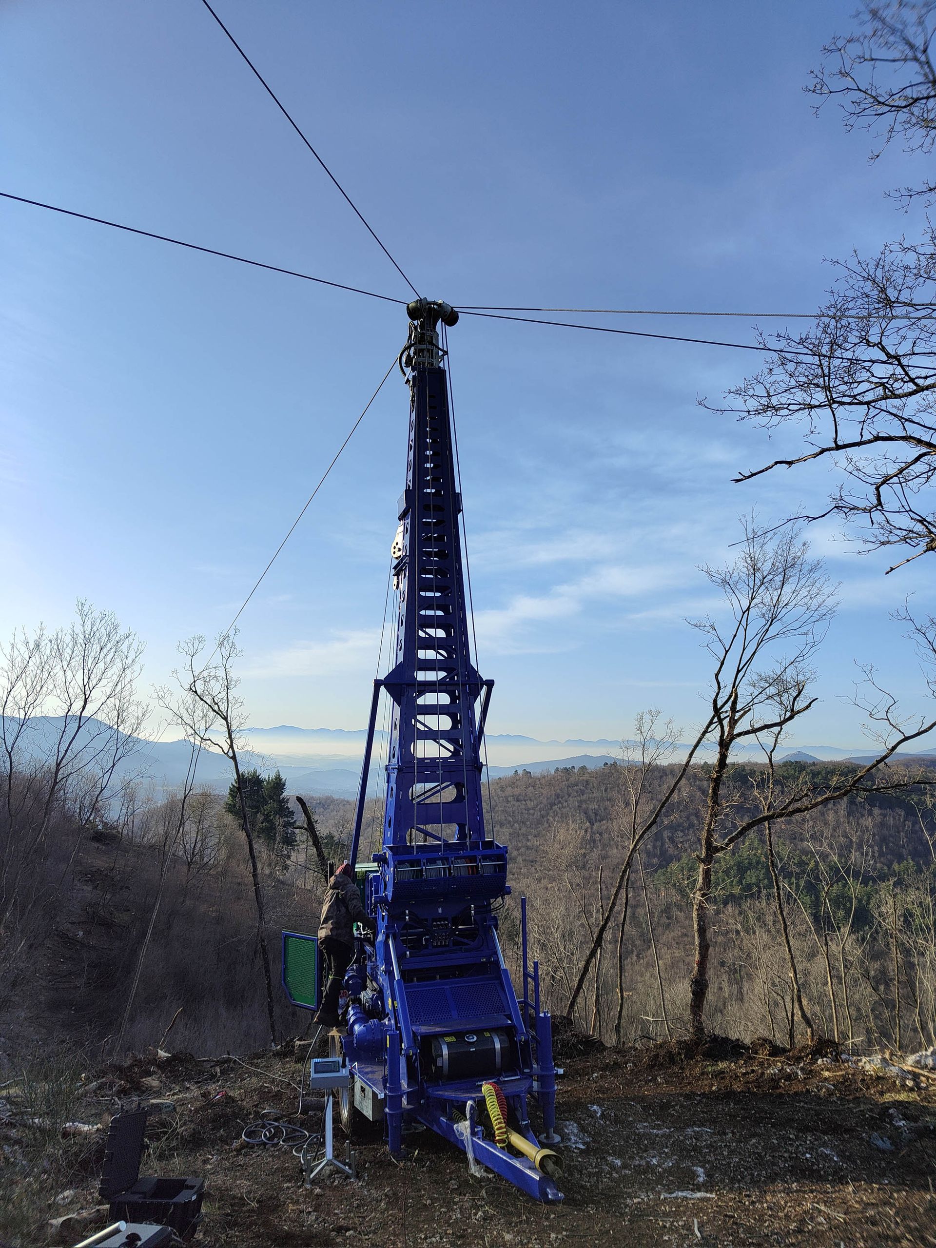 Piattaforma di perforazione blu su una collina contro un cielo azzurro. I cavi si estendono dalla cima.