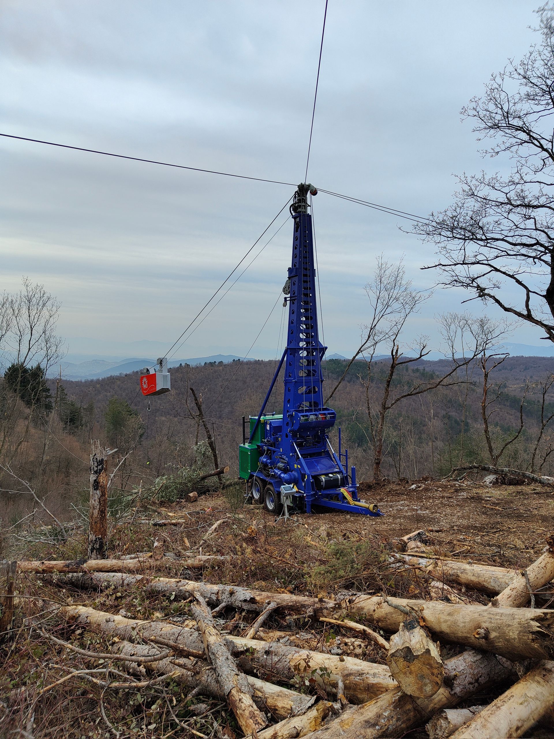 Torre di disboscamento blu in cima a una collina, con un carico sospeso, in funzione in una radura della foresta.