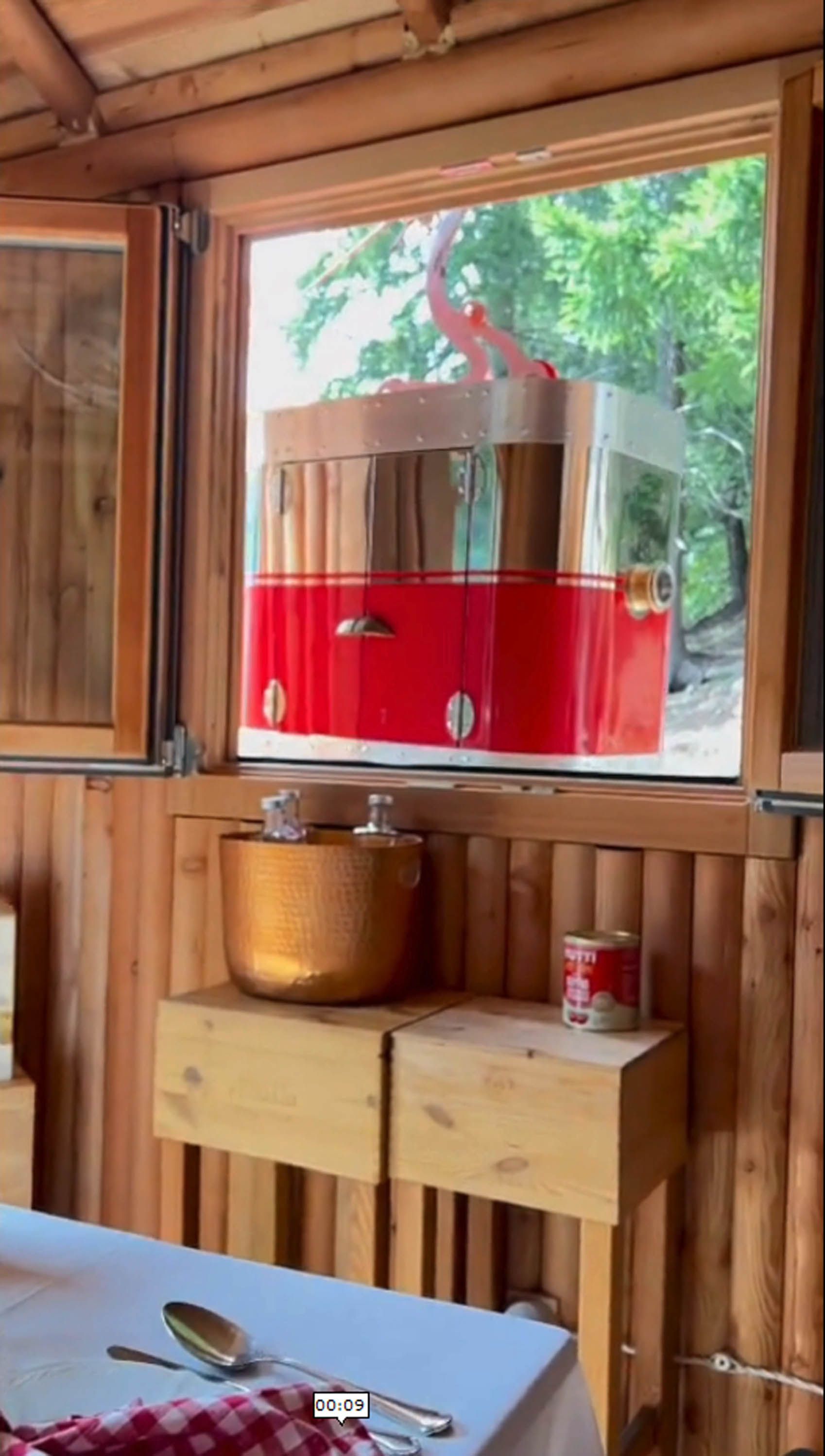 Un tram rosso e di vetro passa davanti a una finestra, all'interno della sala da pranzo di una baita in legno.