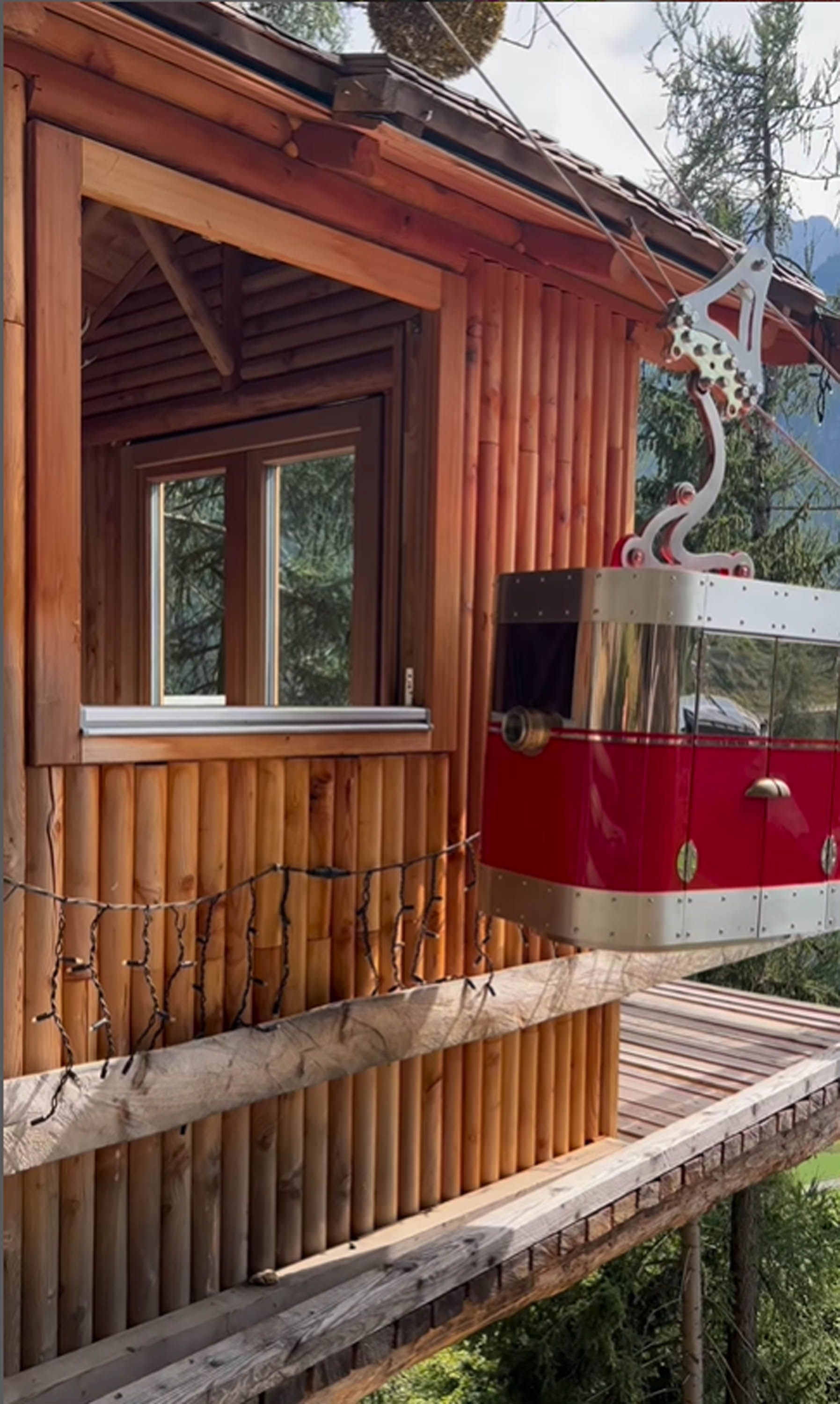 Cabina di legno con funivia rossa, immersa nella foresta.
