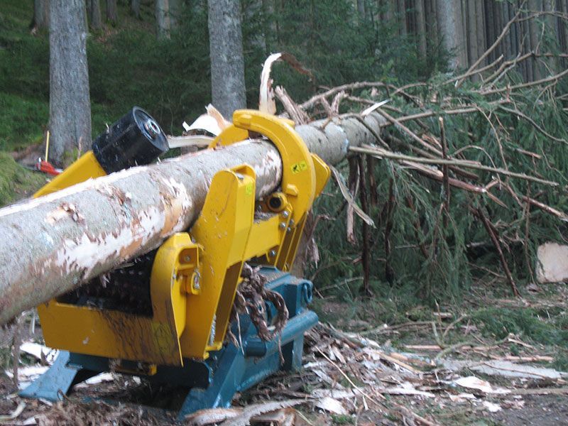 Macchina per la lavorazione dei tronchi gialla e blu con un tronco d'albero in una foresta.