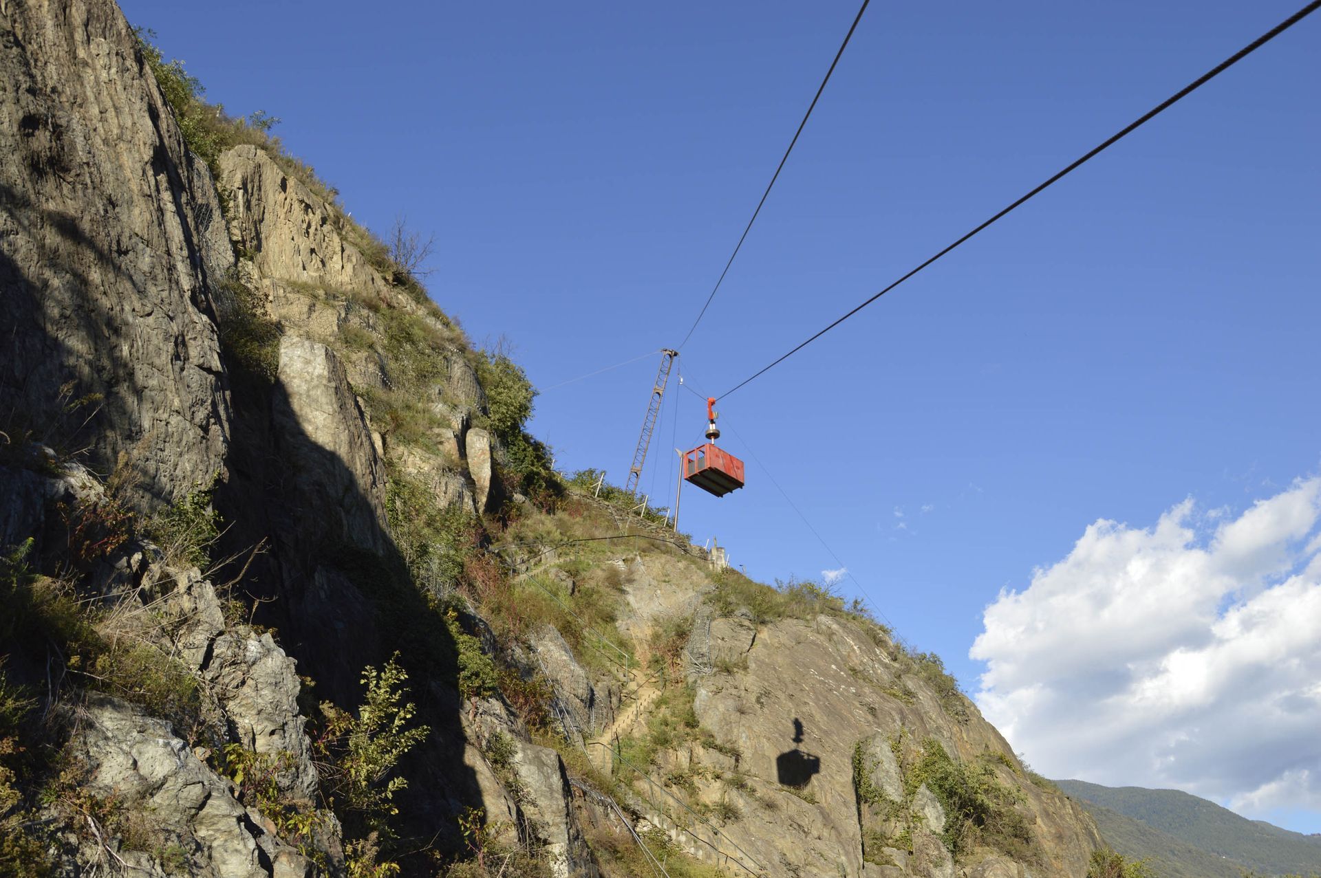 Funivia che sale sul fianco roccioso di una montagna sotto un cielo azzurro e terso.