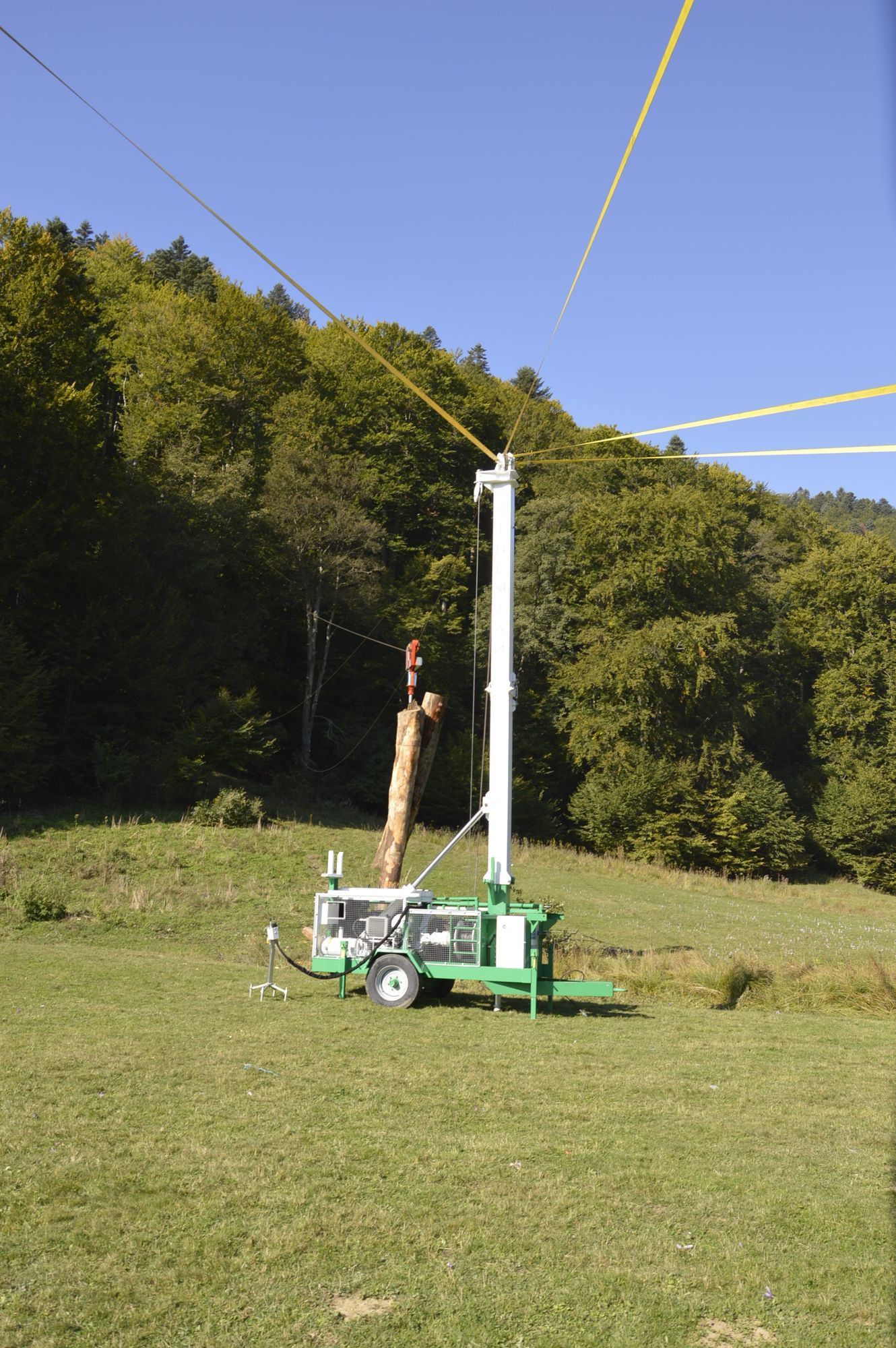 Una torre mobile per il disboscamento in un campo erboso, con un alto albero bianco e alberi sullo sfondo.