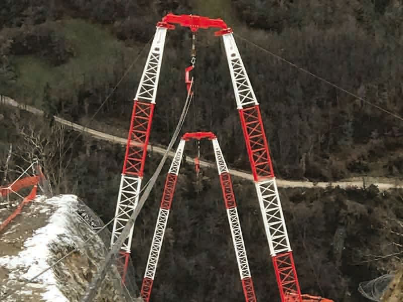 Gru edili rosse e bianche sul fianco di una montagna, probabilmente destinate alla costruzione di un ponte.